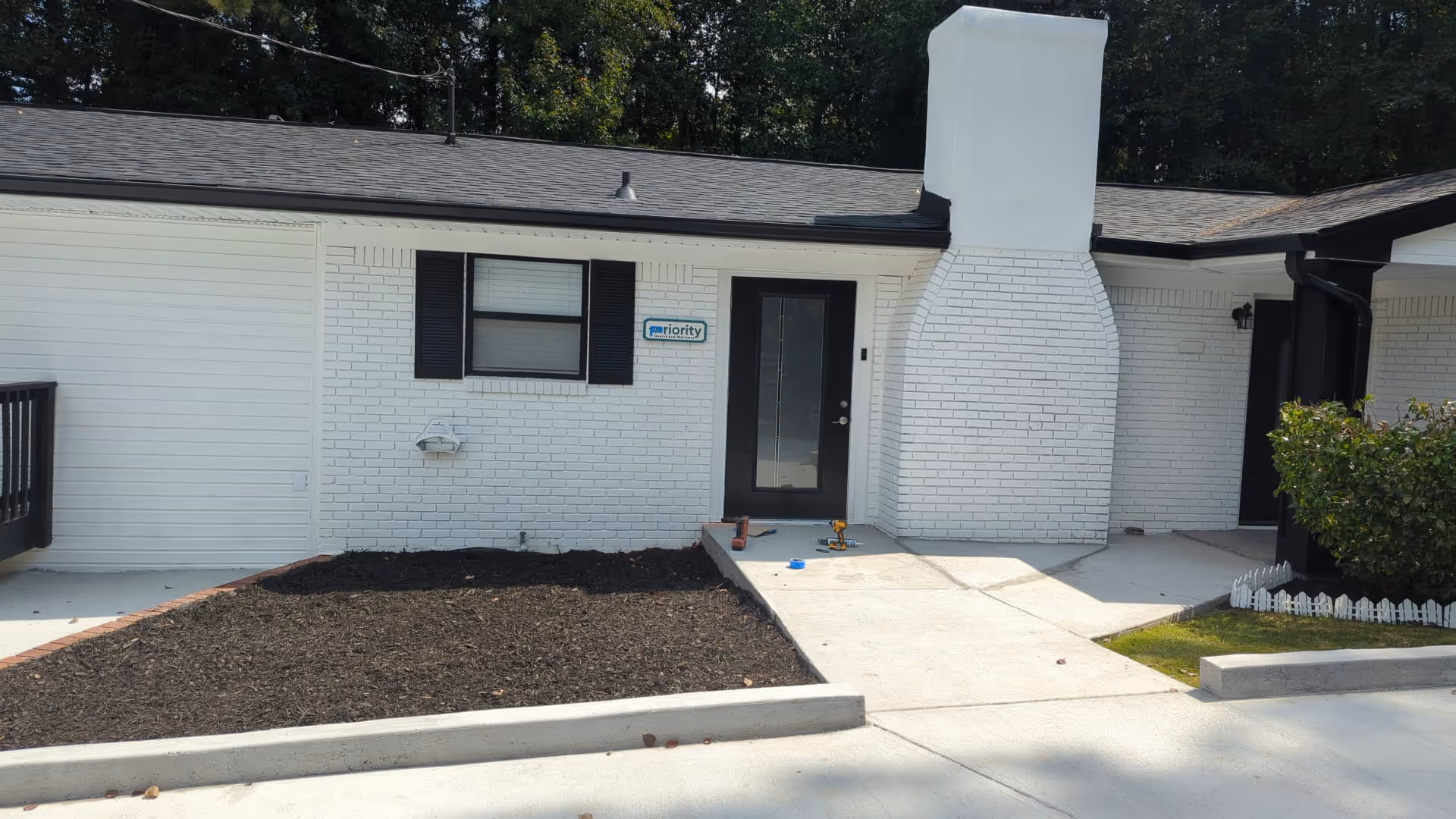 White brick senior living facility exterior featuring a front door, concrete walkway, and small landscaped area.