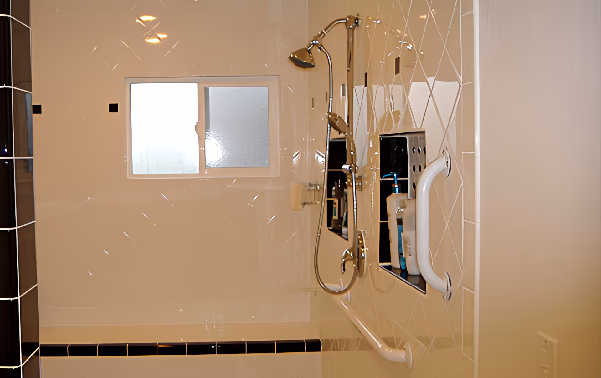 Shower stall with a handheld showerhead, grab bars, a built-in niche with toiletries, and a frosted window.