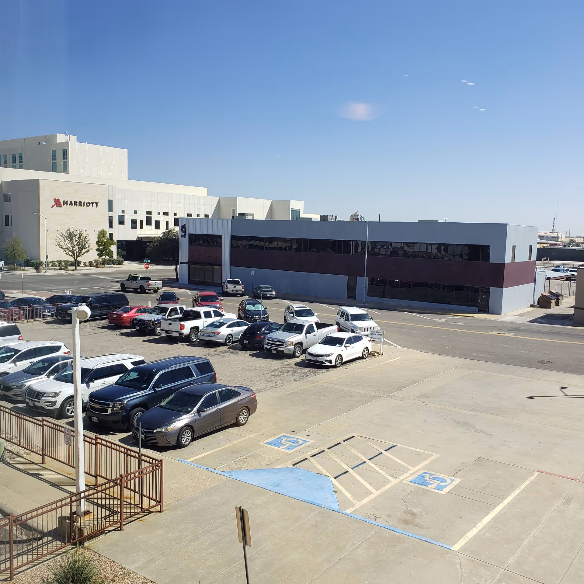 Wide view of a parking lot with modern buildings under a clear blue sky.