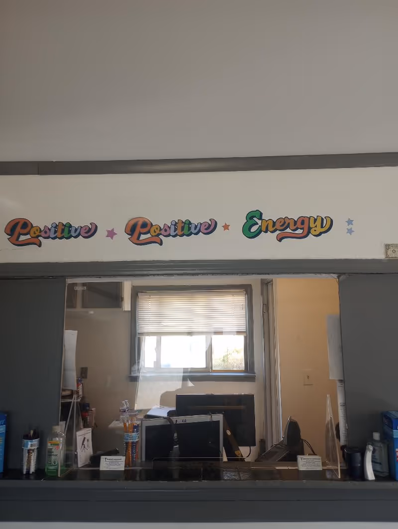 Reception window behind a glass divider with a colorful 'Positive Energy' sign on the wall.