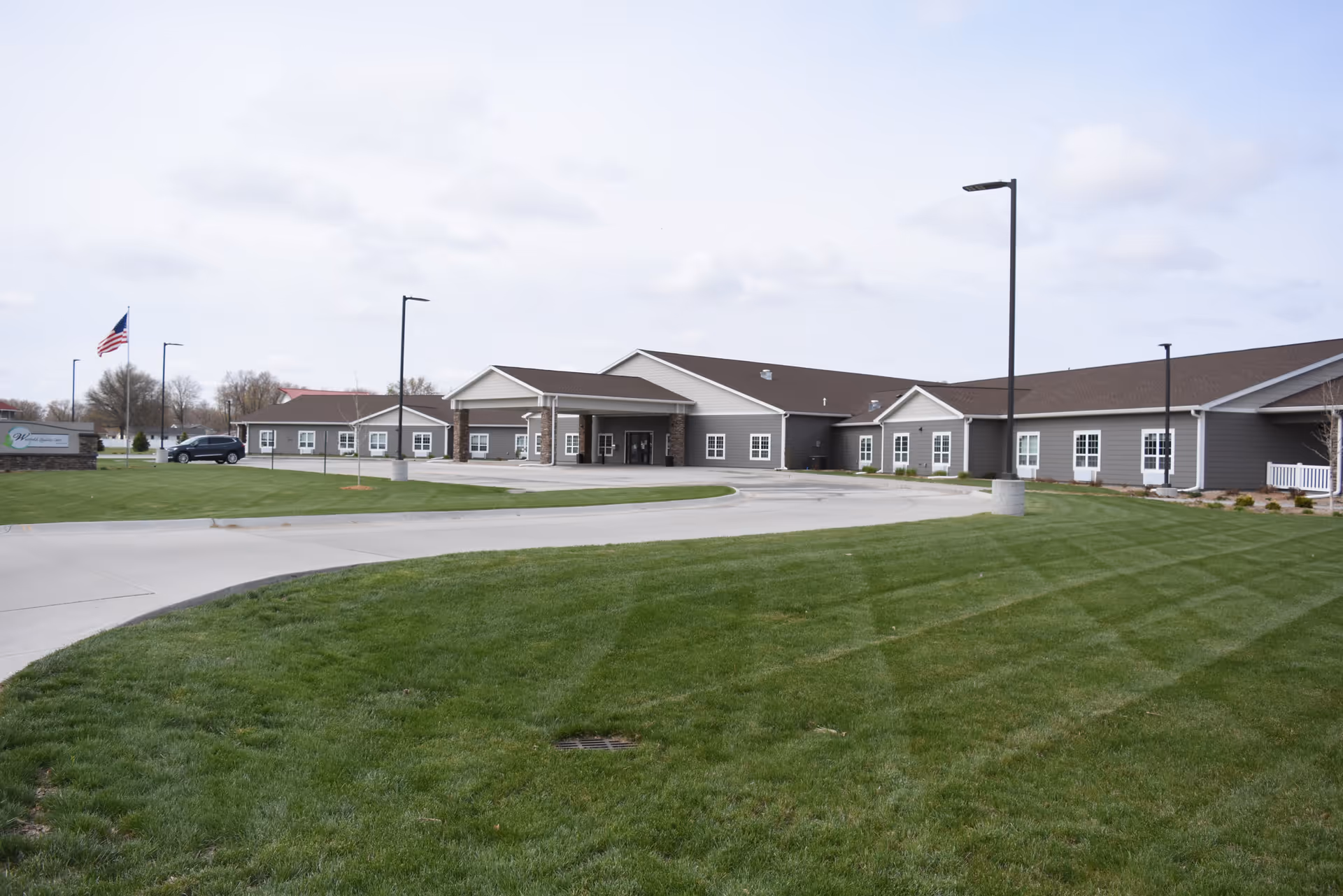 Single-story assisted living facility with gray siding, entrance, and well-kept green lawn