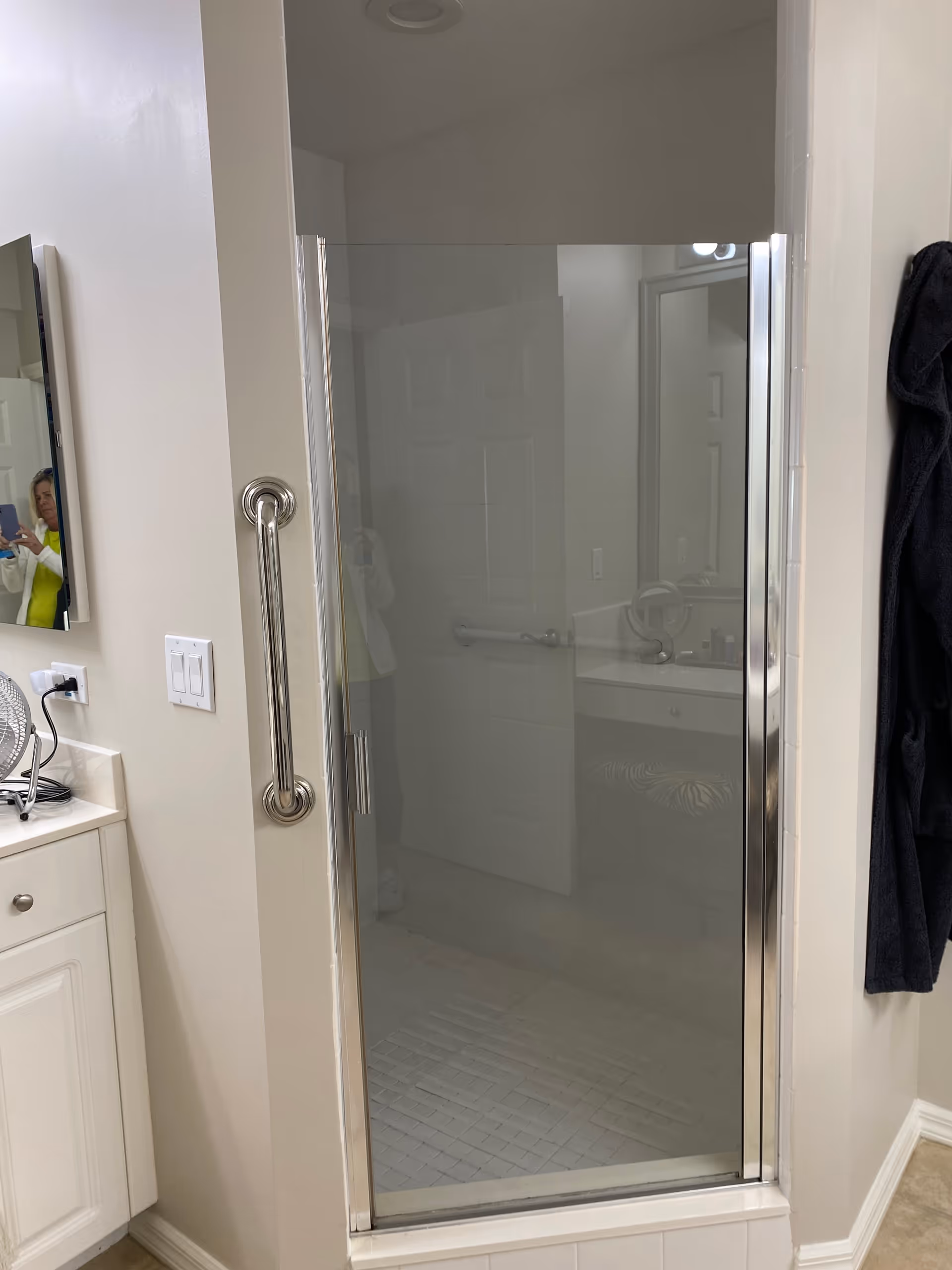 Accessible bathroom with glass shower door, grab bar, and vanity mirror.