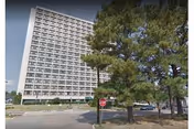 Tall, multi-story building with trees and a street in the foreground.