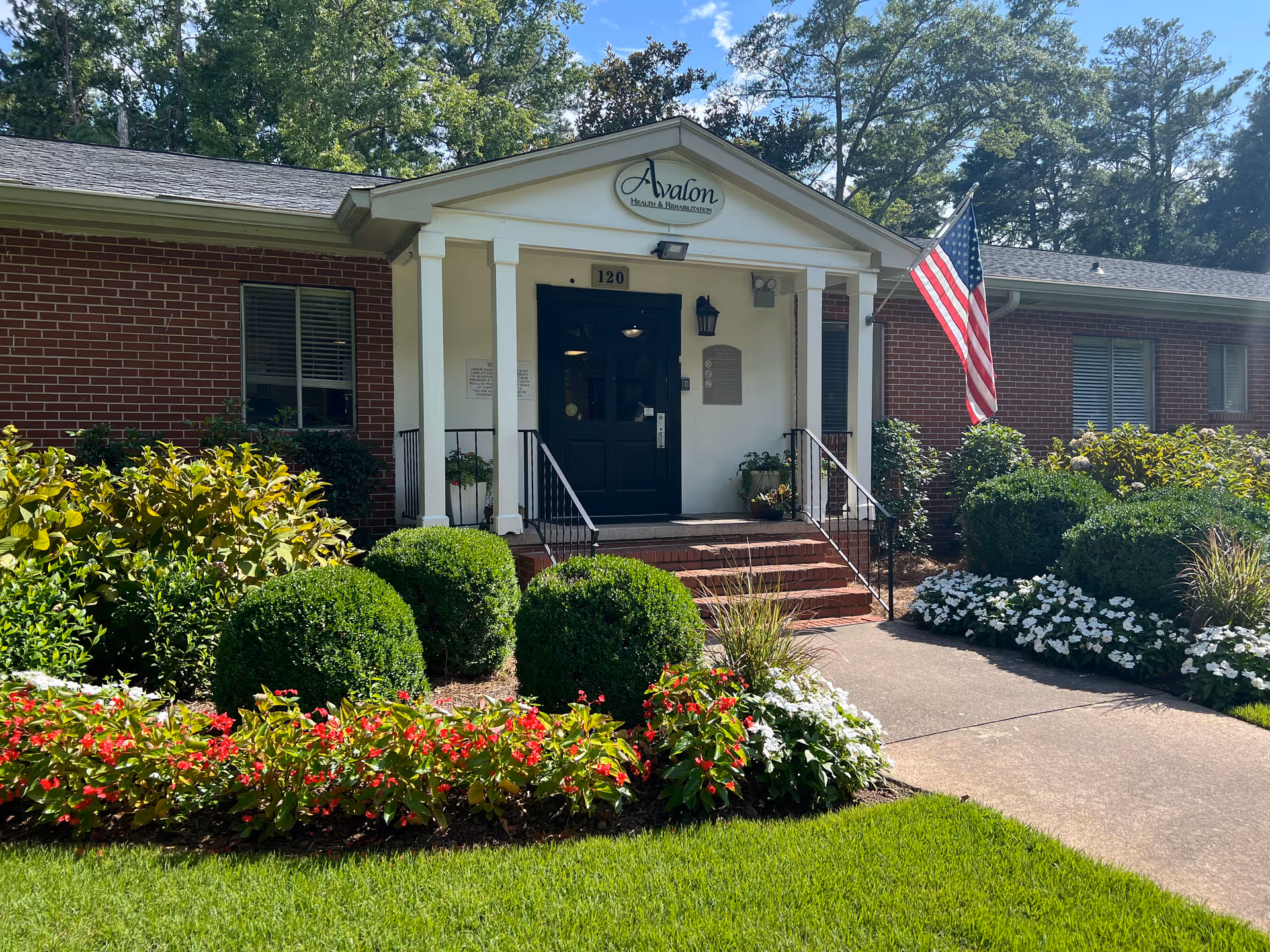 Front entrance of Avalon Health & Rehabilitation framed by manicured shrubs and flowers.