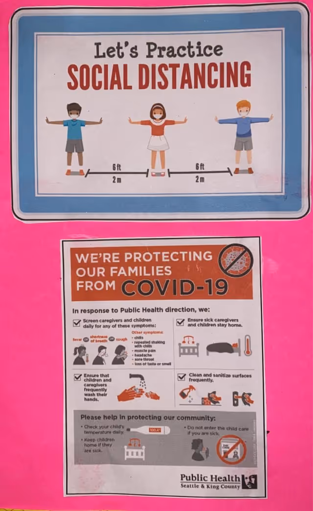 A bright pink wall features social distancing and COVID-19 safety posters.