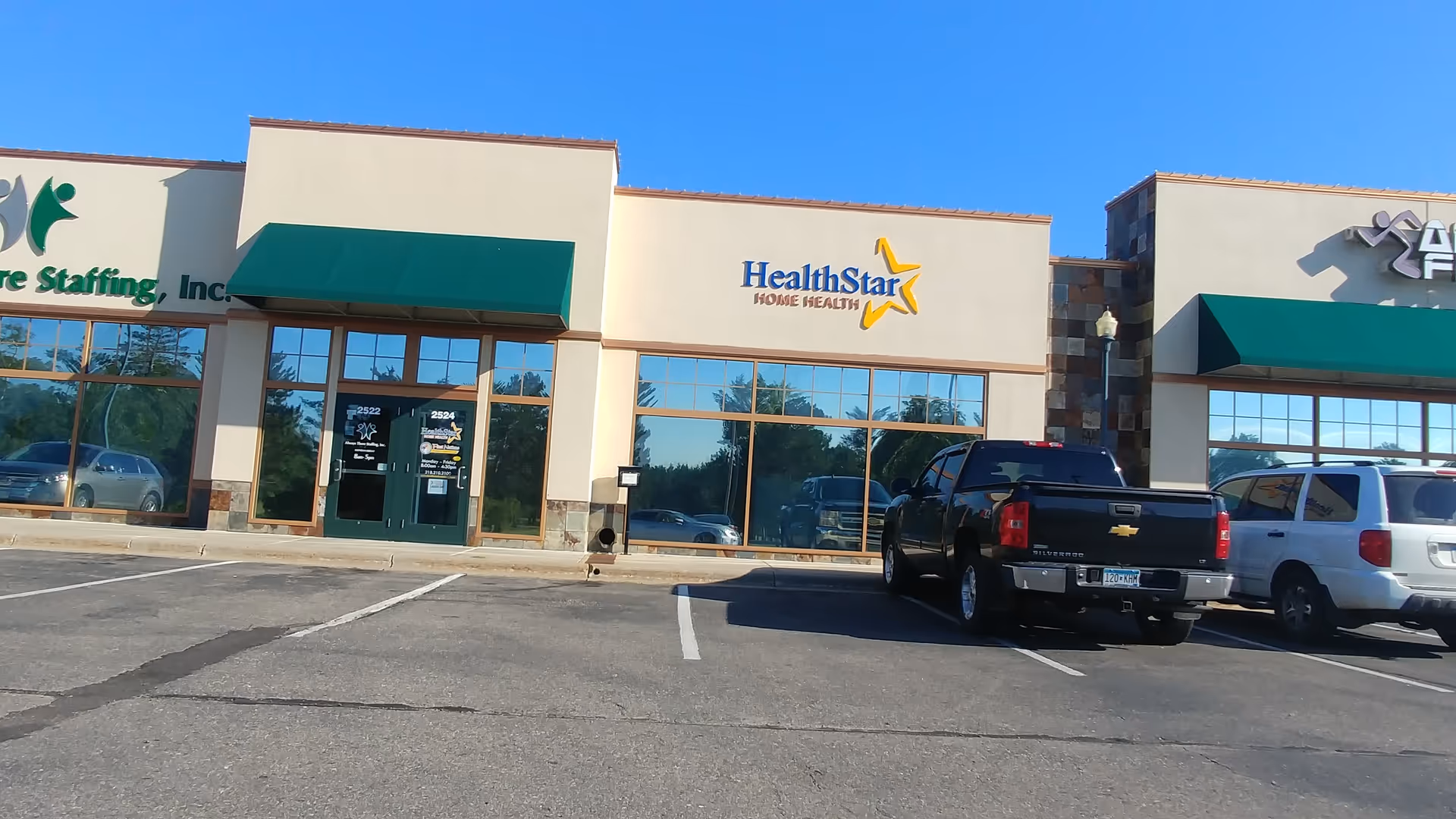 Exterior storefronts of a strip mall with HealthStar Home Health sign and parked vehicles.