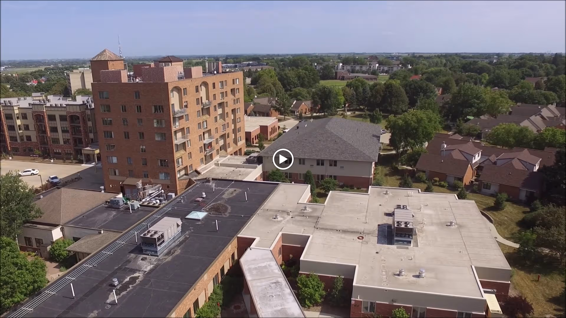 Aerial view of Green Hills Health Care Center showing multiple connected buildings with flat roofs, surrounded by trees and residential houses under a clear sky.