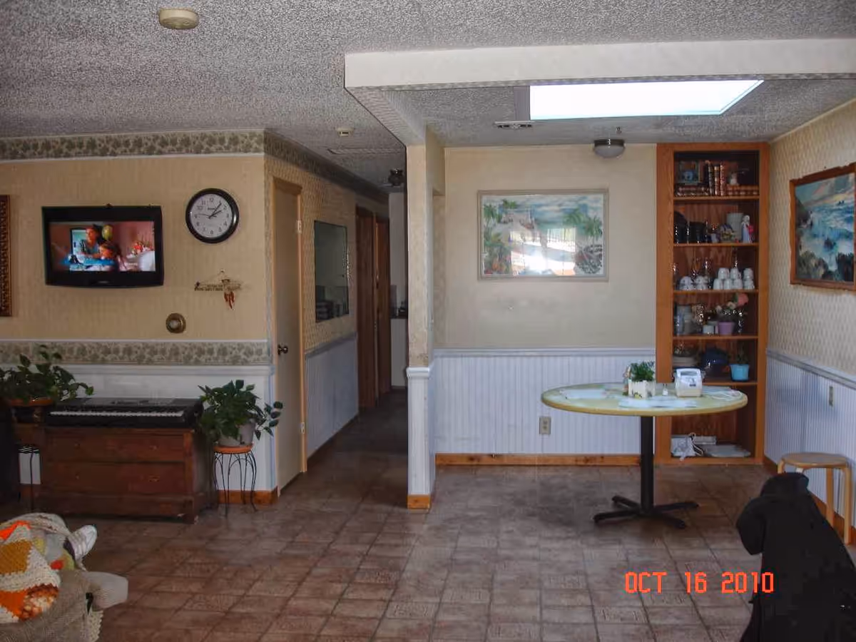 A cozy interior common area with a round table, piano, and shelf display.
