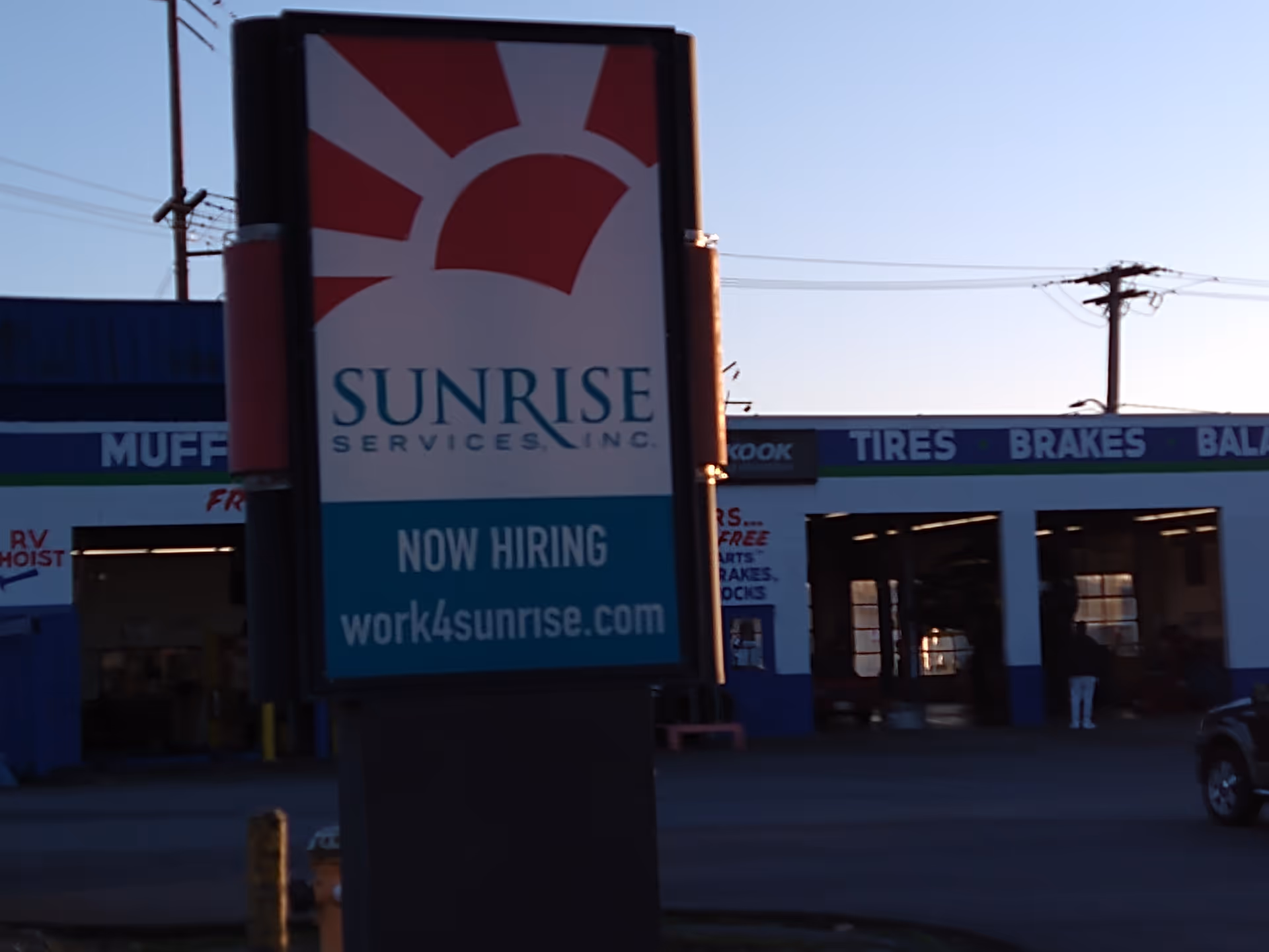 A large Sunrise sign outside a service shop with Now Hiring text.
