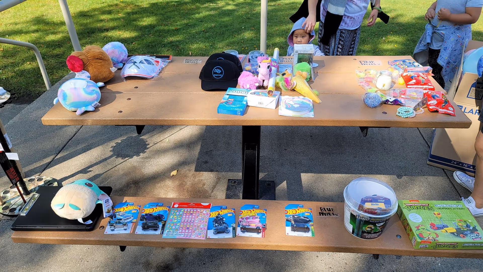 Outdoor display table filled with toys, plushies, and trinkets under a canopy.