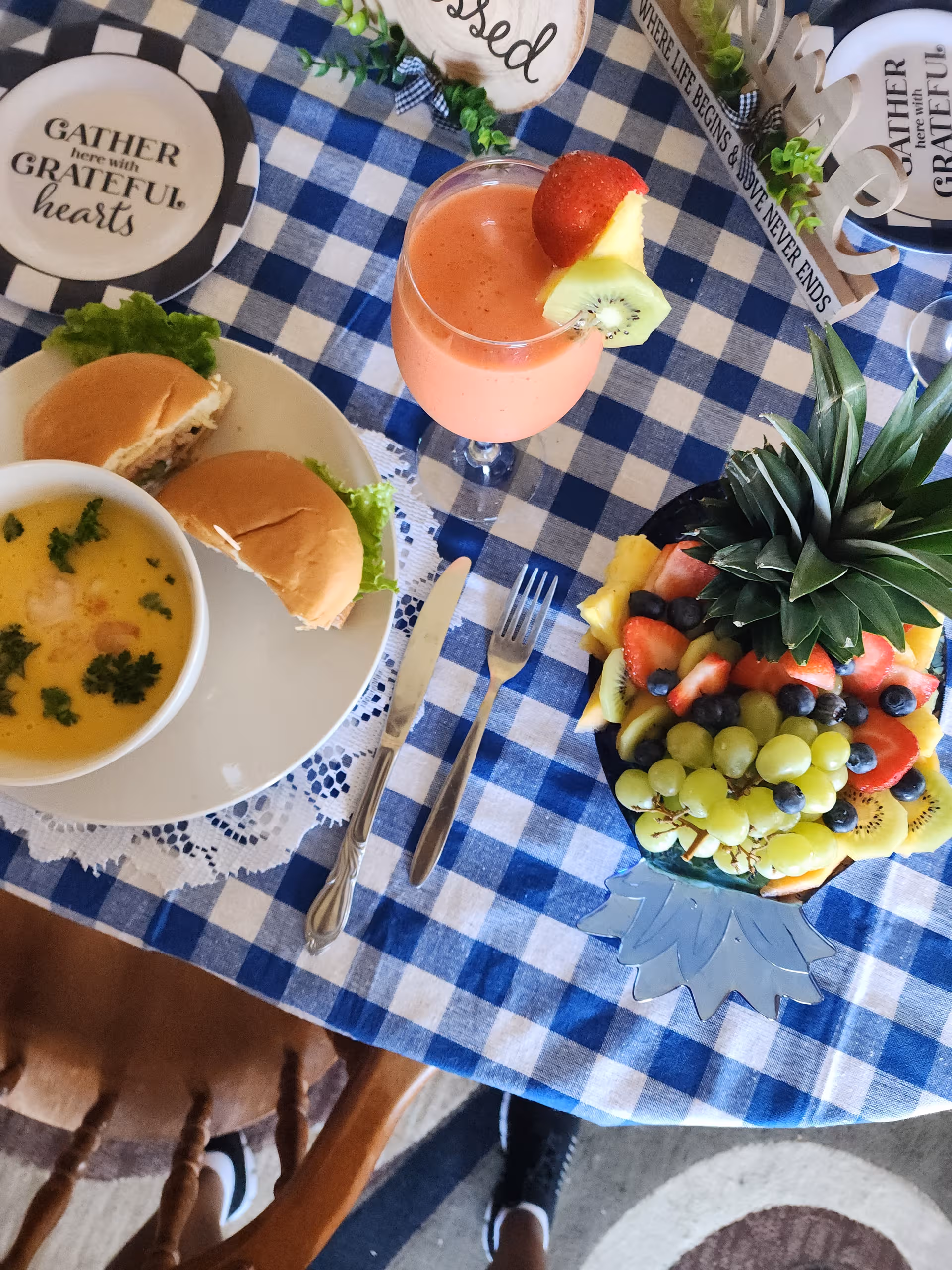 Dining table set for a meal with soup, sliders, fruit platter, and pink beverage.