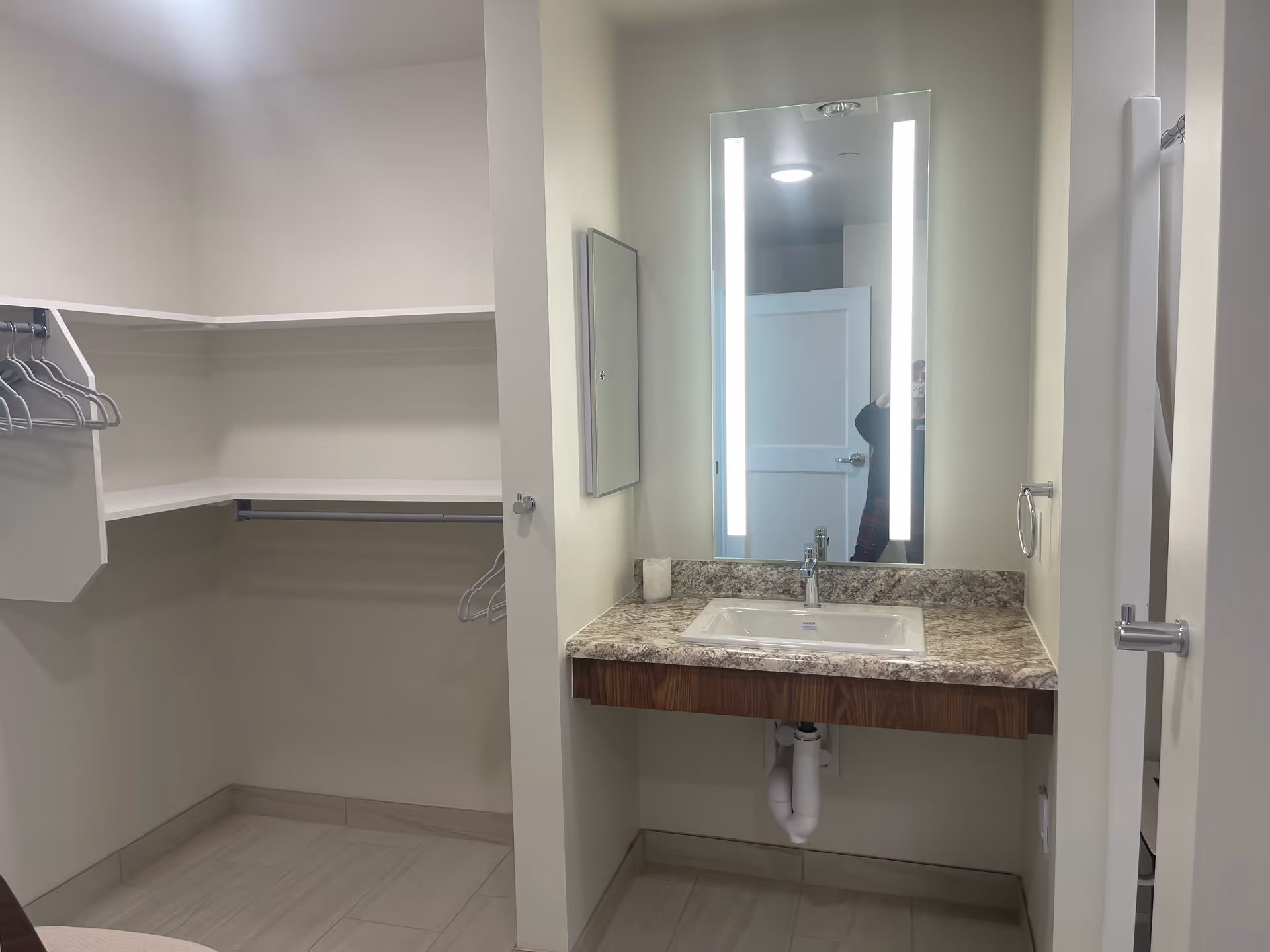 Bathroom vanity with granite countertop, illuminated mirror, and open closet area to the left.