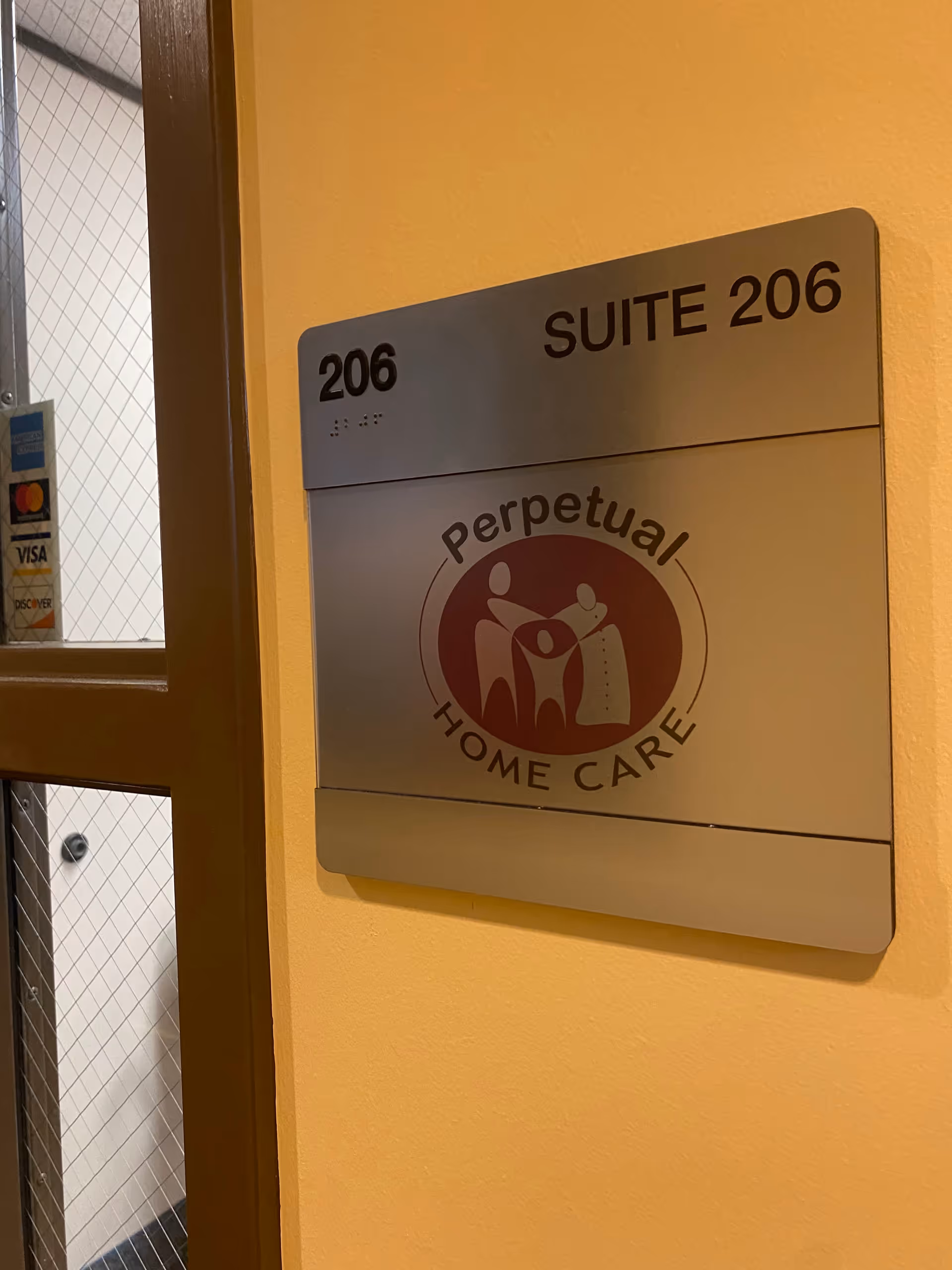 Wall-mounted metal sign labeled Suite 206 and Perpetual Home Care on a yellow wall.