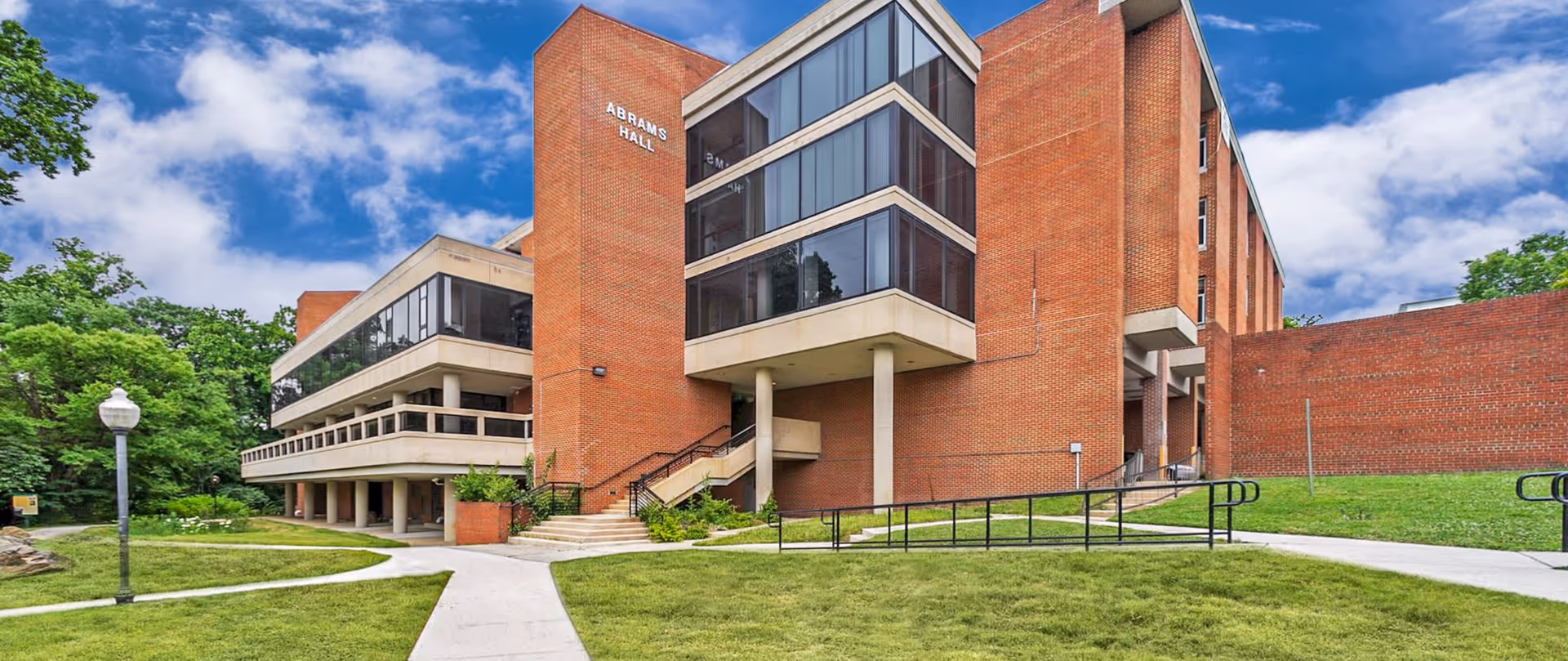 Brick Abrams Hall Senior Apartments exterior with lawn, walkway, and stair entrance.