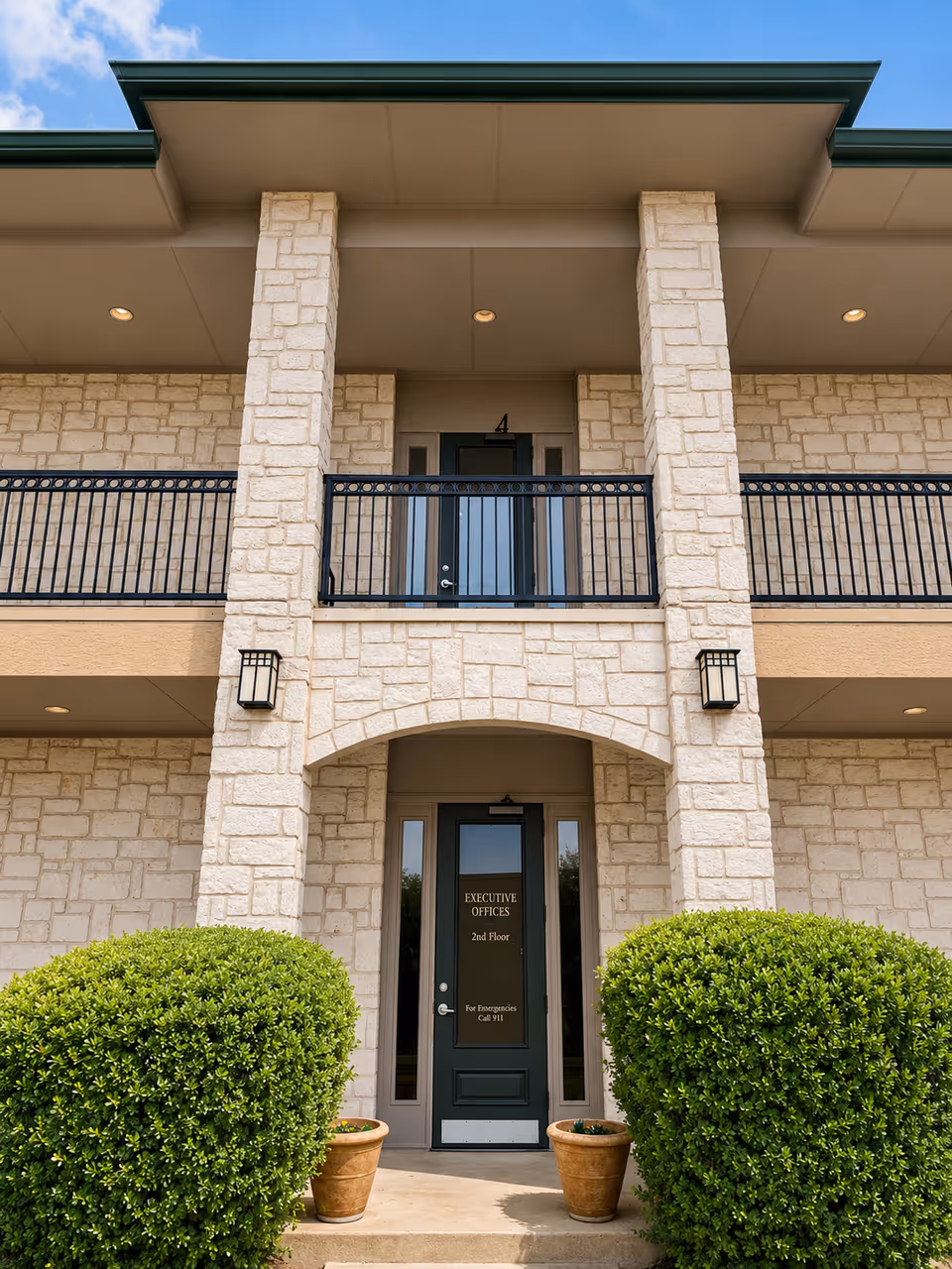 Stone exterior with a central arched doorway labeled Executive Offices, second-floor balcony, and greenery.