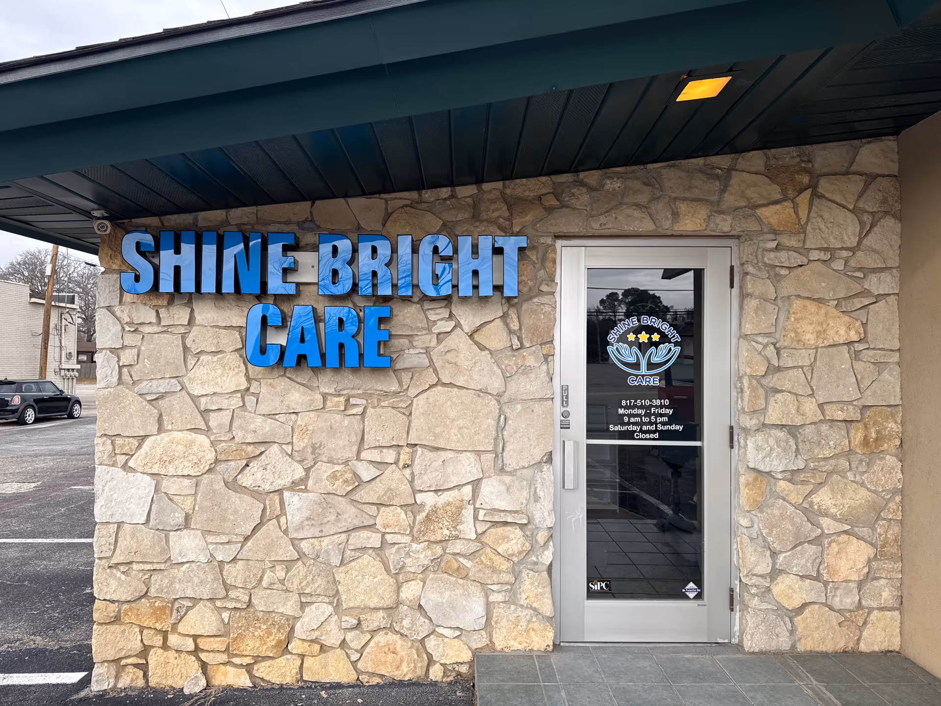 Exterior of Shine Bright Care facility with a stone facade, blue sign letters, and glass door.