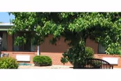 Exterior view of North Adams Home brick facility with trees, shrubs, and a bench.