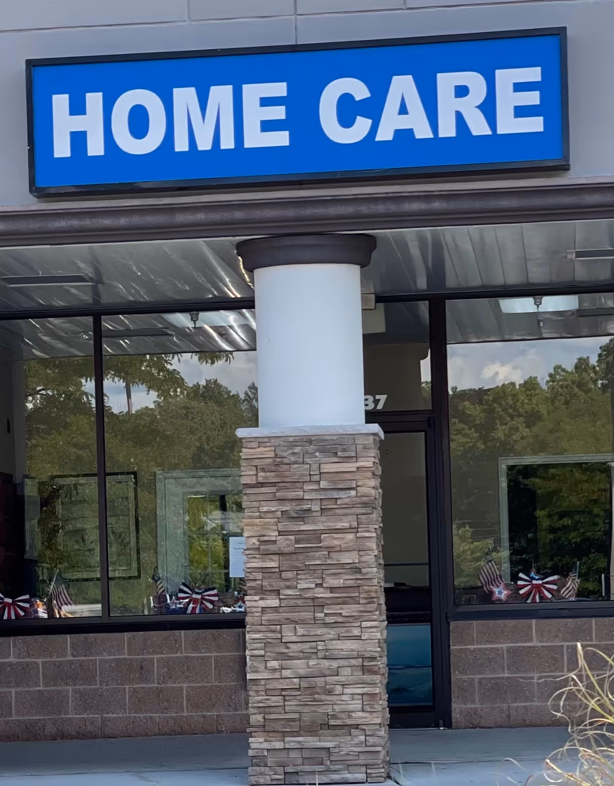 Exterior building entrance with a blue HOME CARE sign and stone pillar.