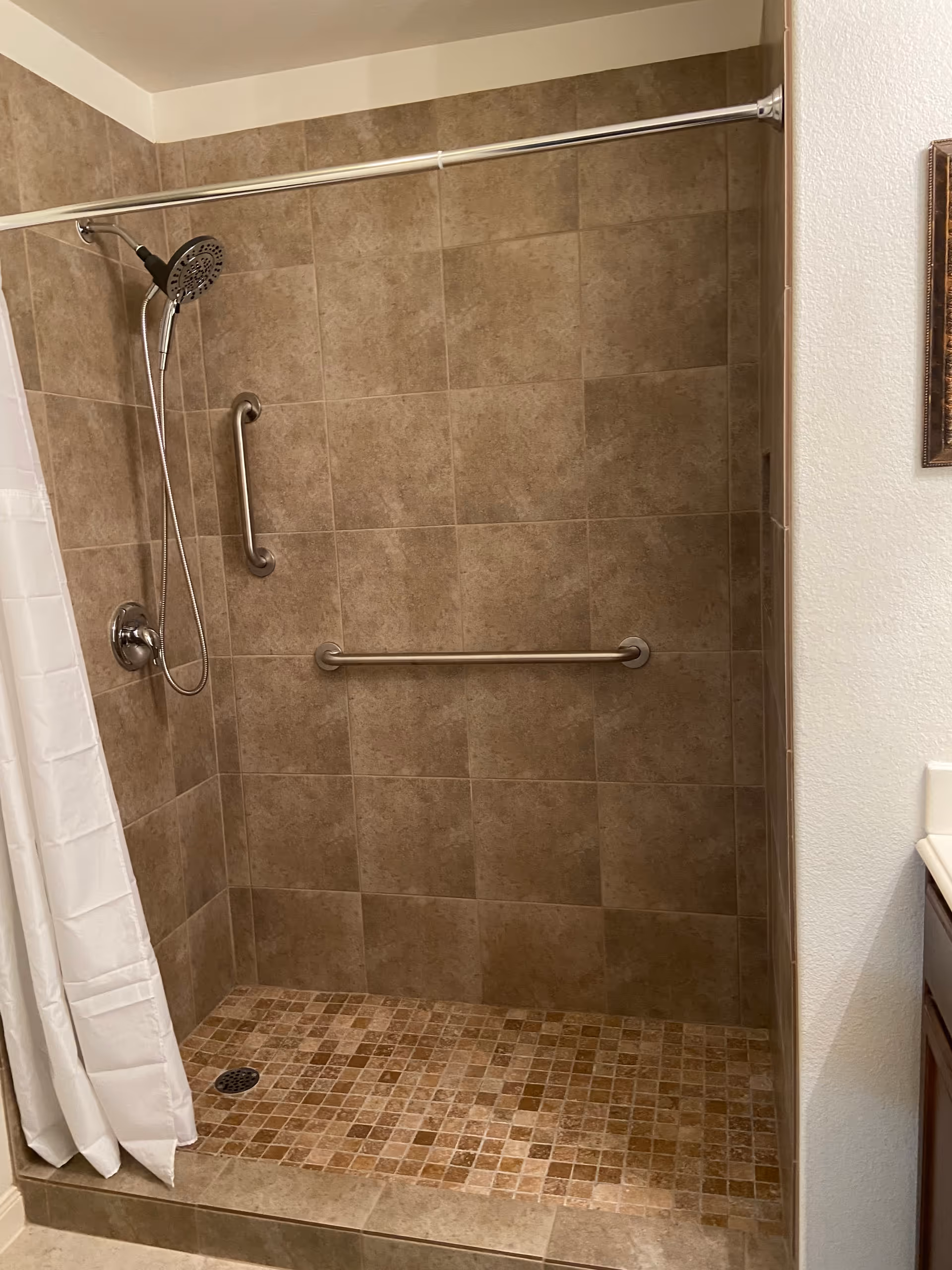 Accessible bathroom shower with tiled walls, grab bars, and a curtain.