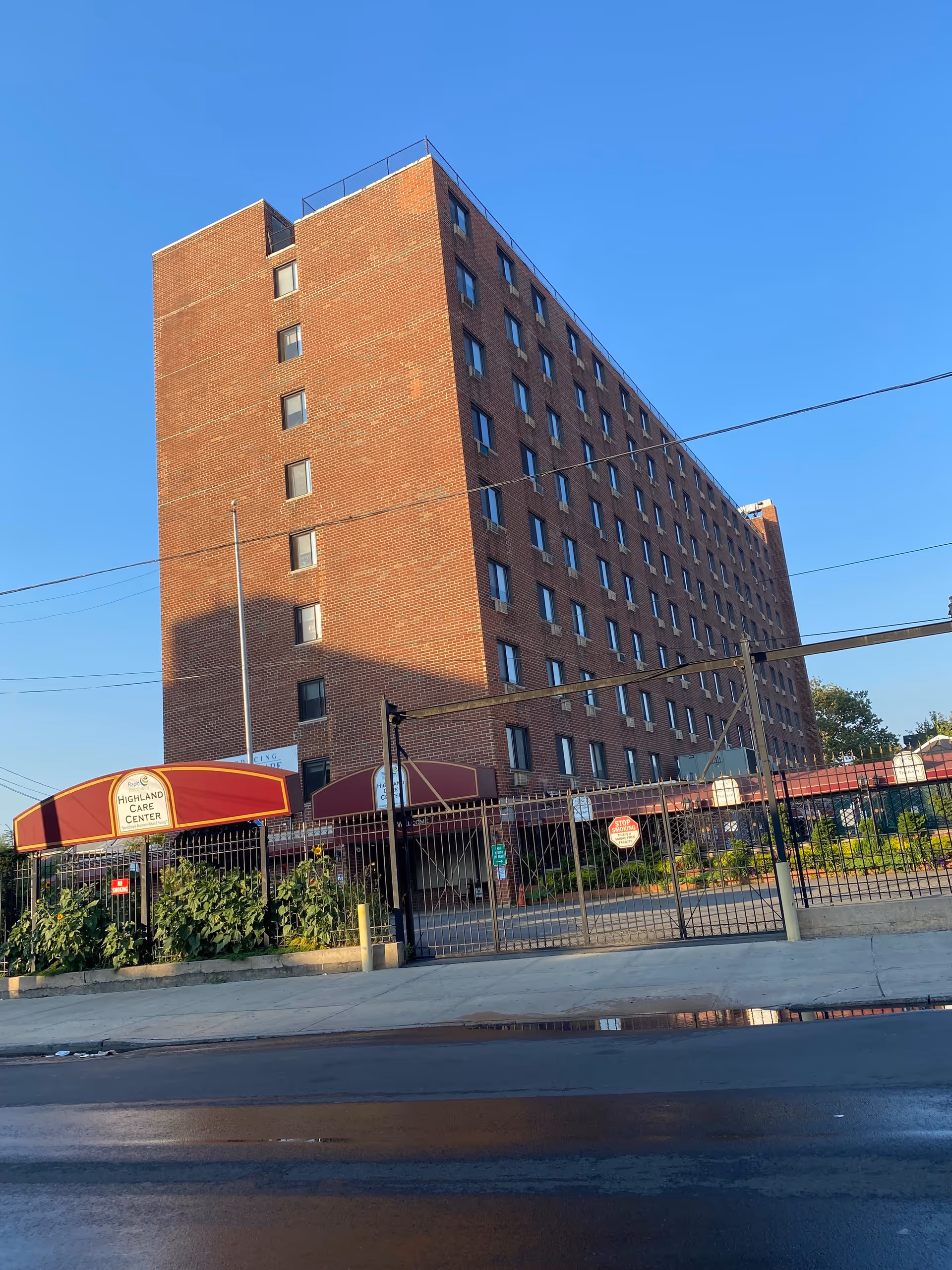 Tall brick senior care building with Highland Care Center sign and gated entrance along street.