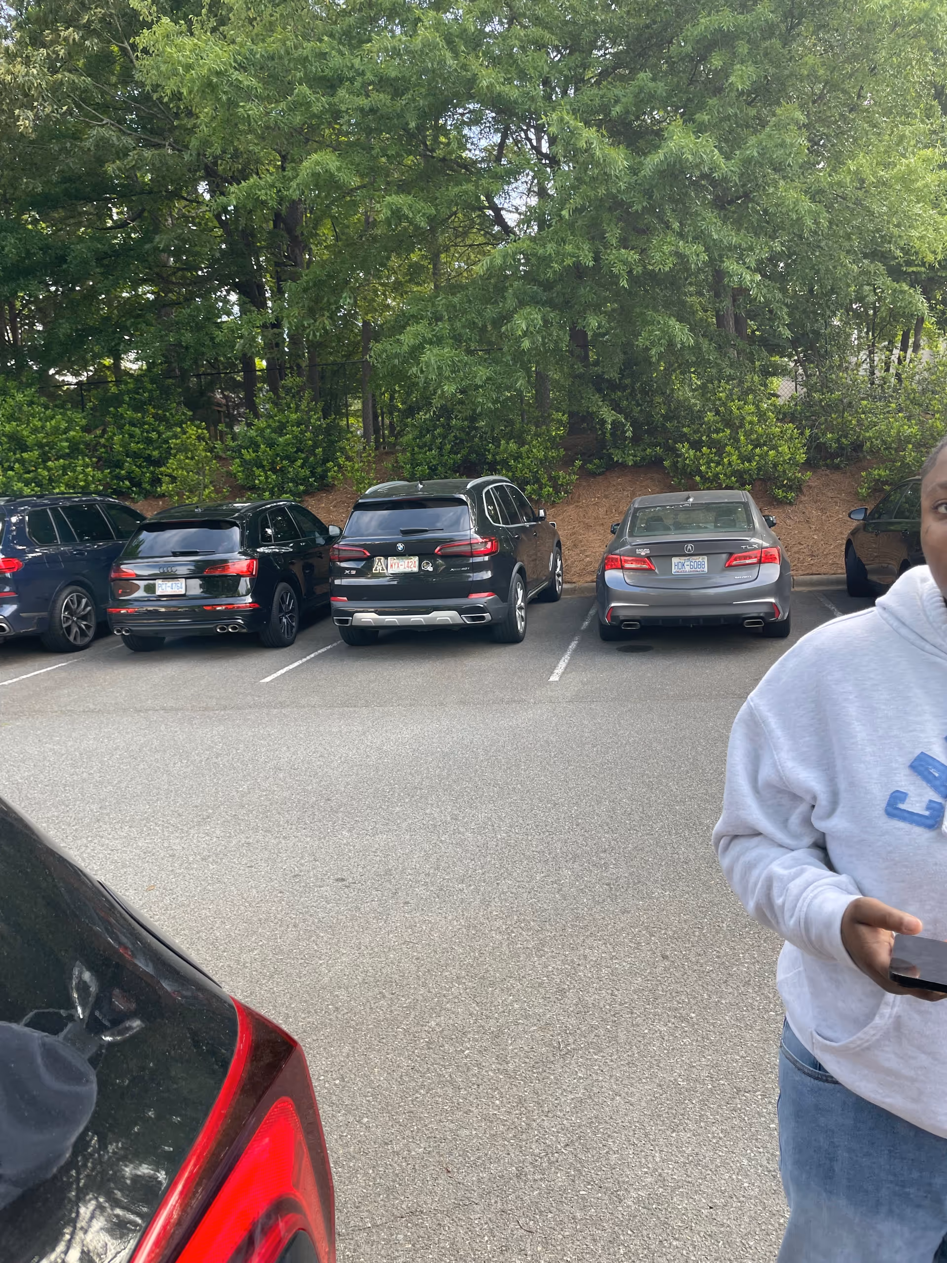 Parking lot with several cars lined up and a person in a gray hoodie at right.