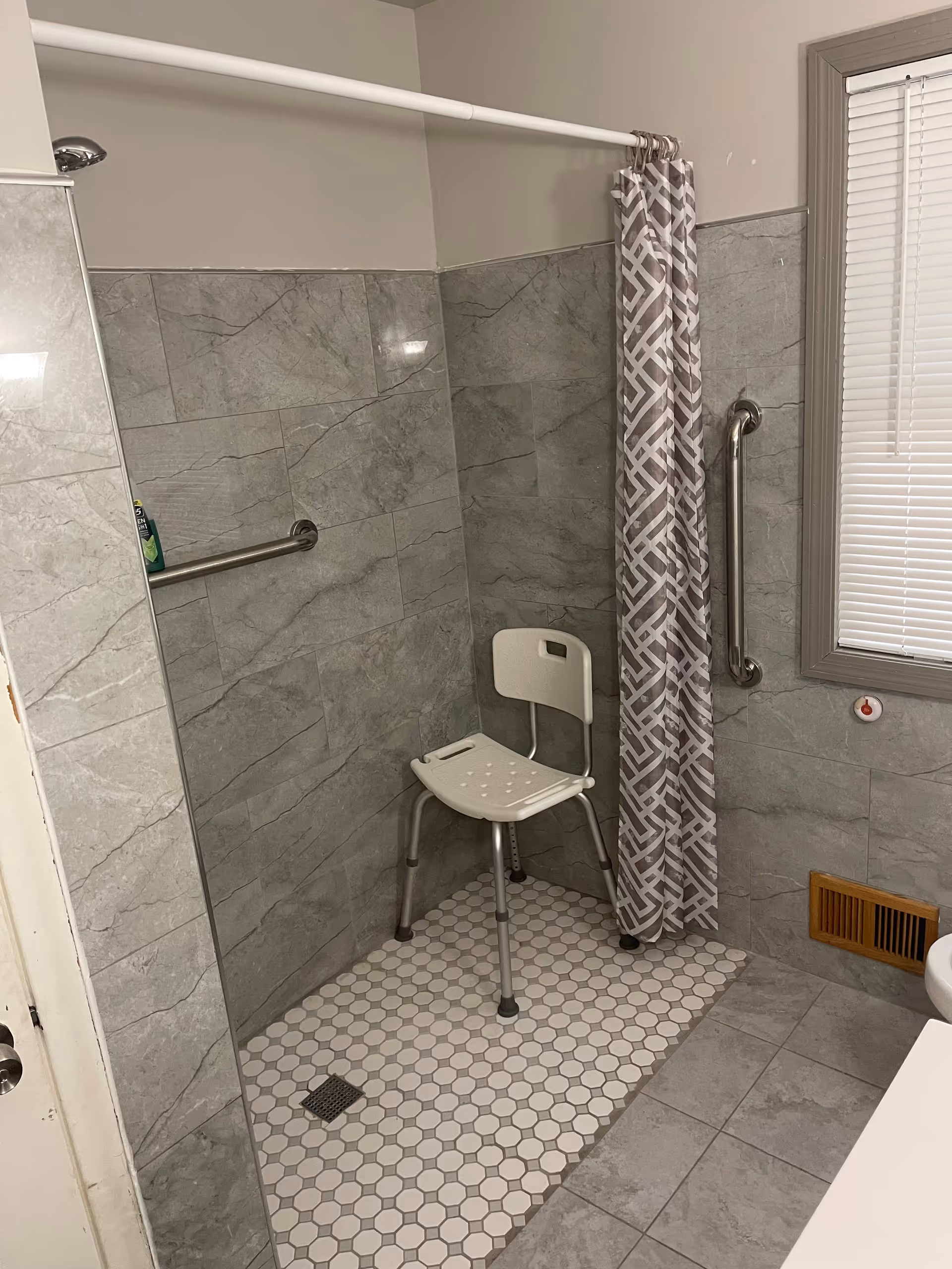 Accessible bathroom in a senior facility with a shower chair and grab bars.