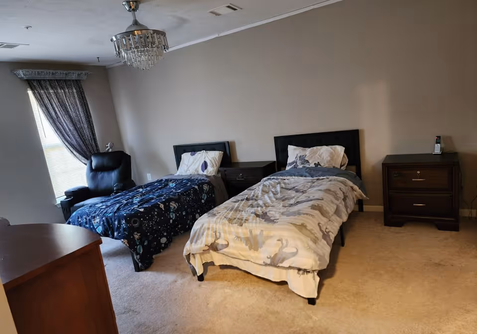 Two twin beds with dark headboards and a chair, nightstands, and window curtains in a bedroom.
