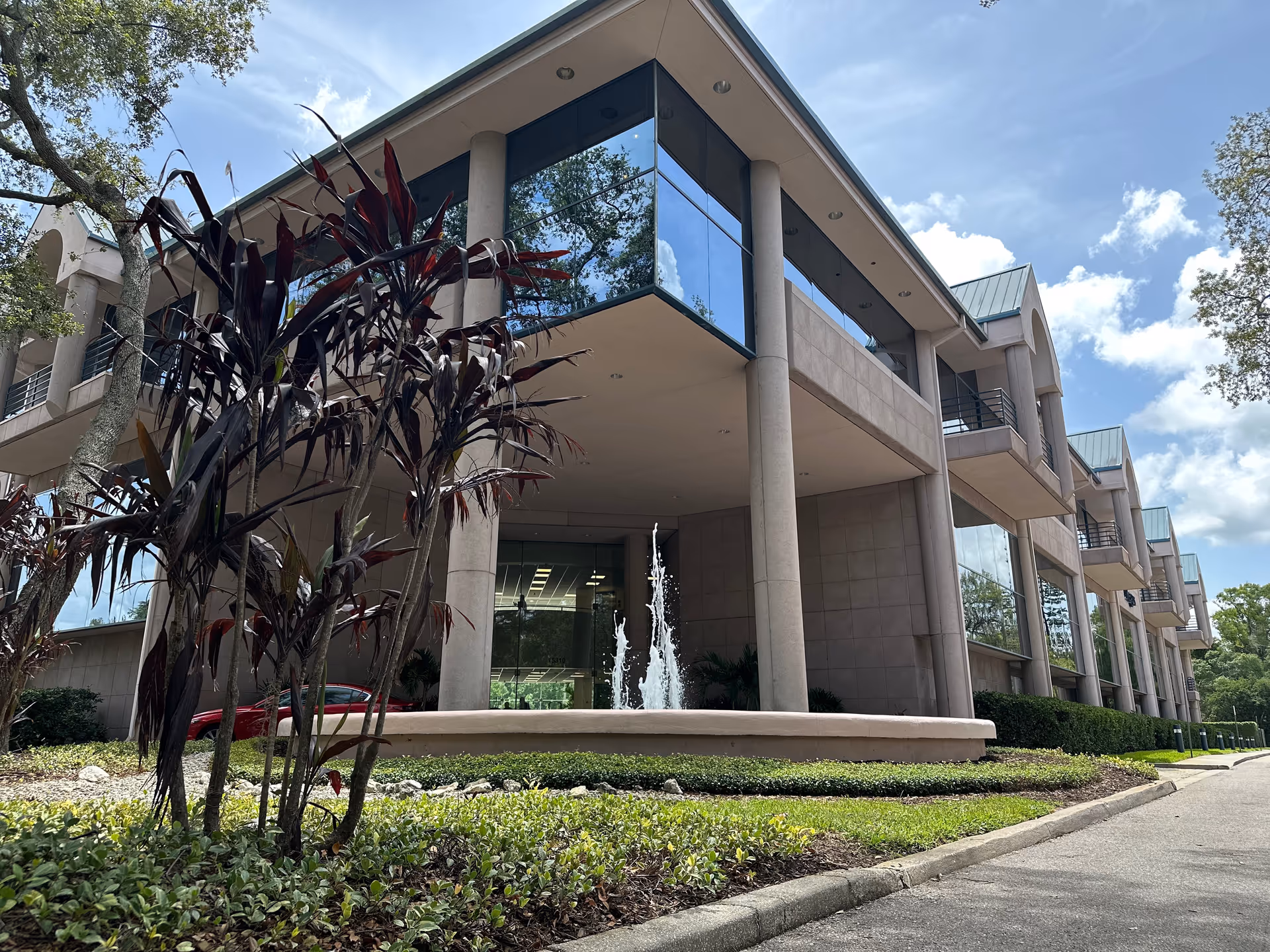 Modern senior living facility exterior with glass balconies and a central fountain.