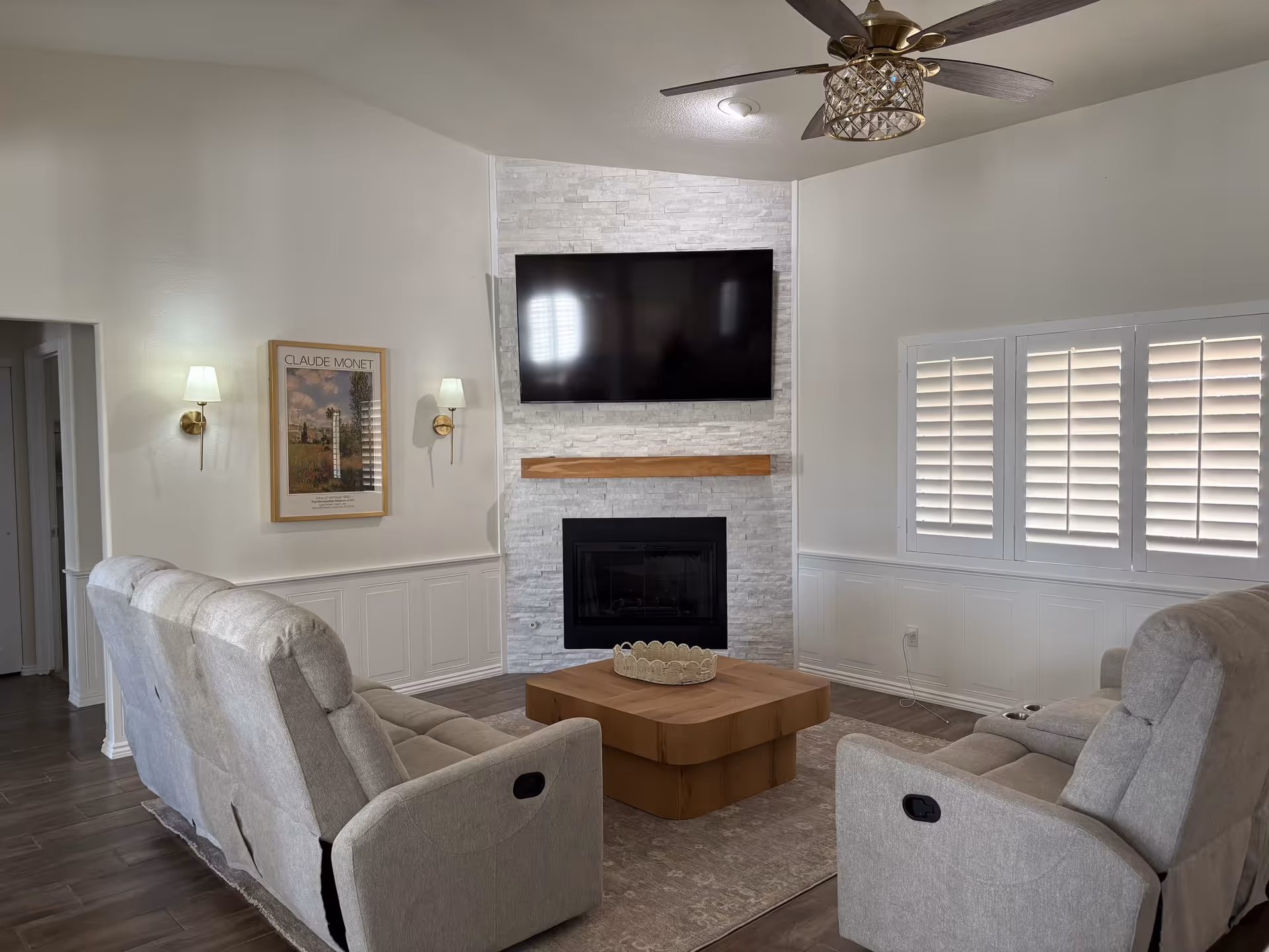 Neutral living room with fireplace, mounted TV, two recliners, and window shutters.