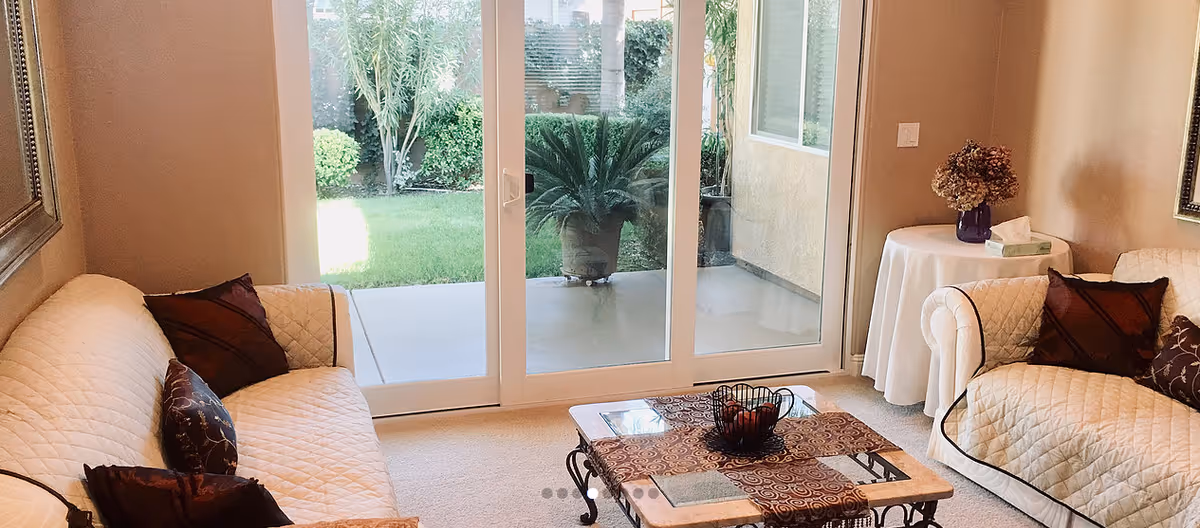 Sunlit living room with white quilted sofas, a coffee table, and glass doors to a patio.
