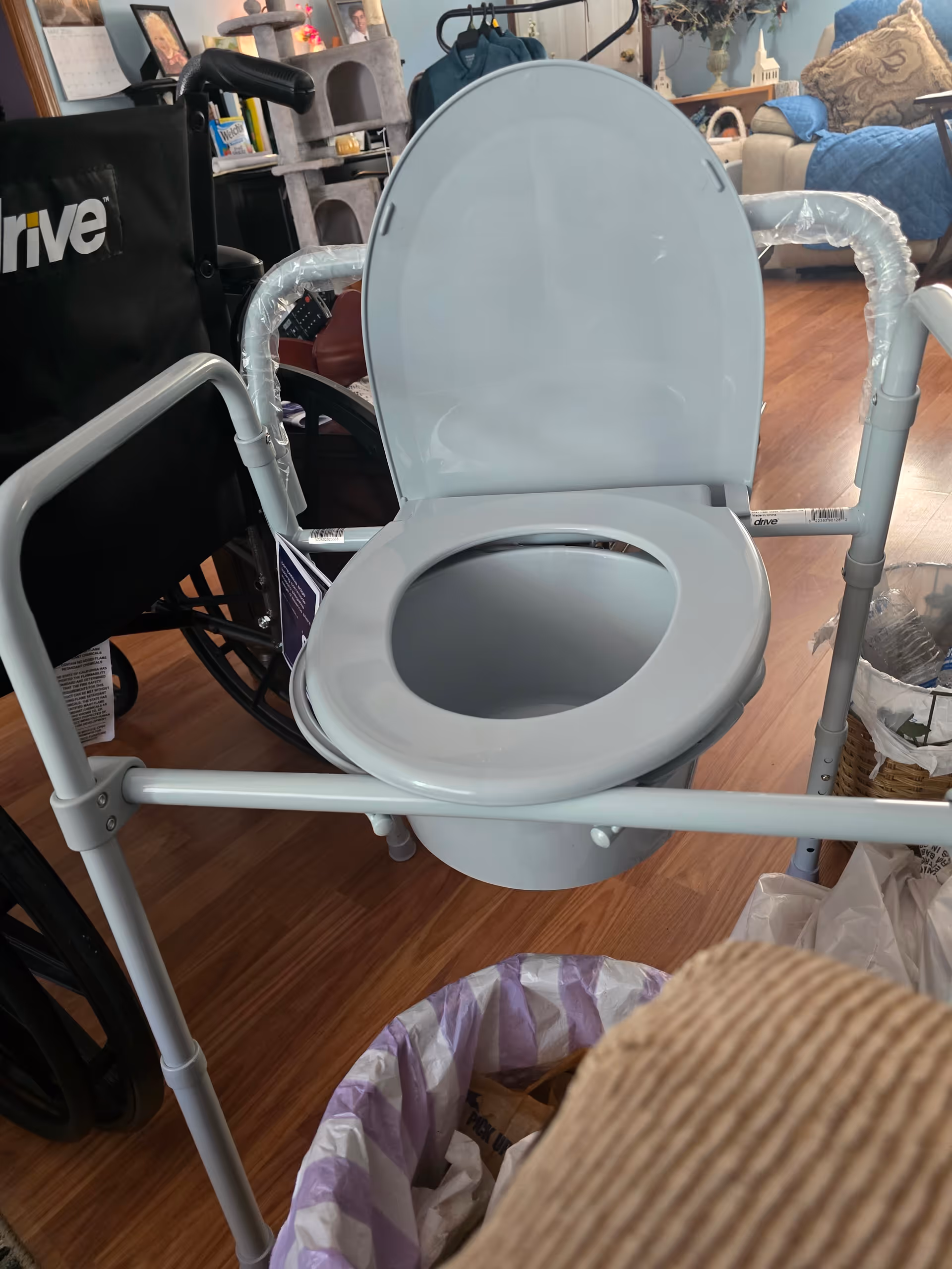 Gray elevated toilet seat with safety rails, part of mobility equipment in room.