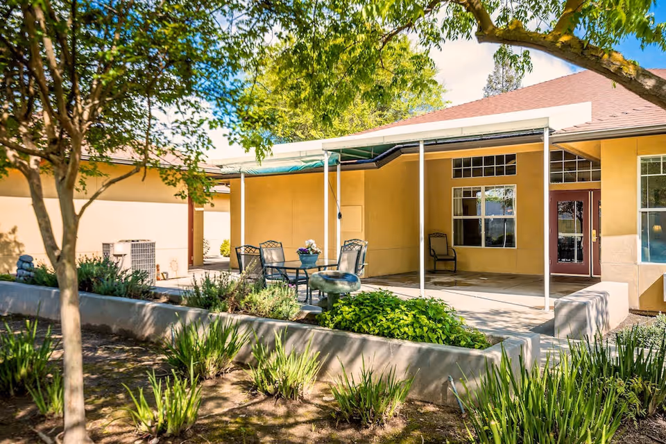 Outdoor patio at The Gardens of Modesto featuring seating and a yellow building.