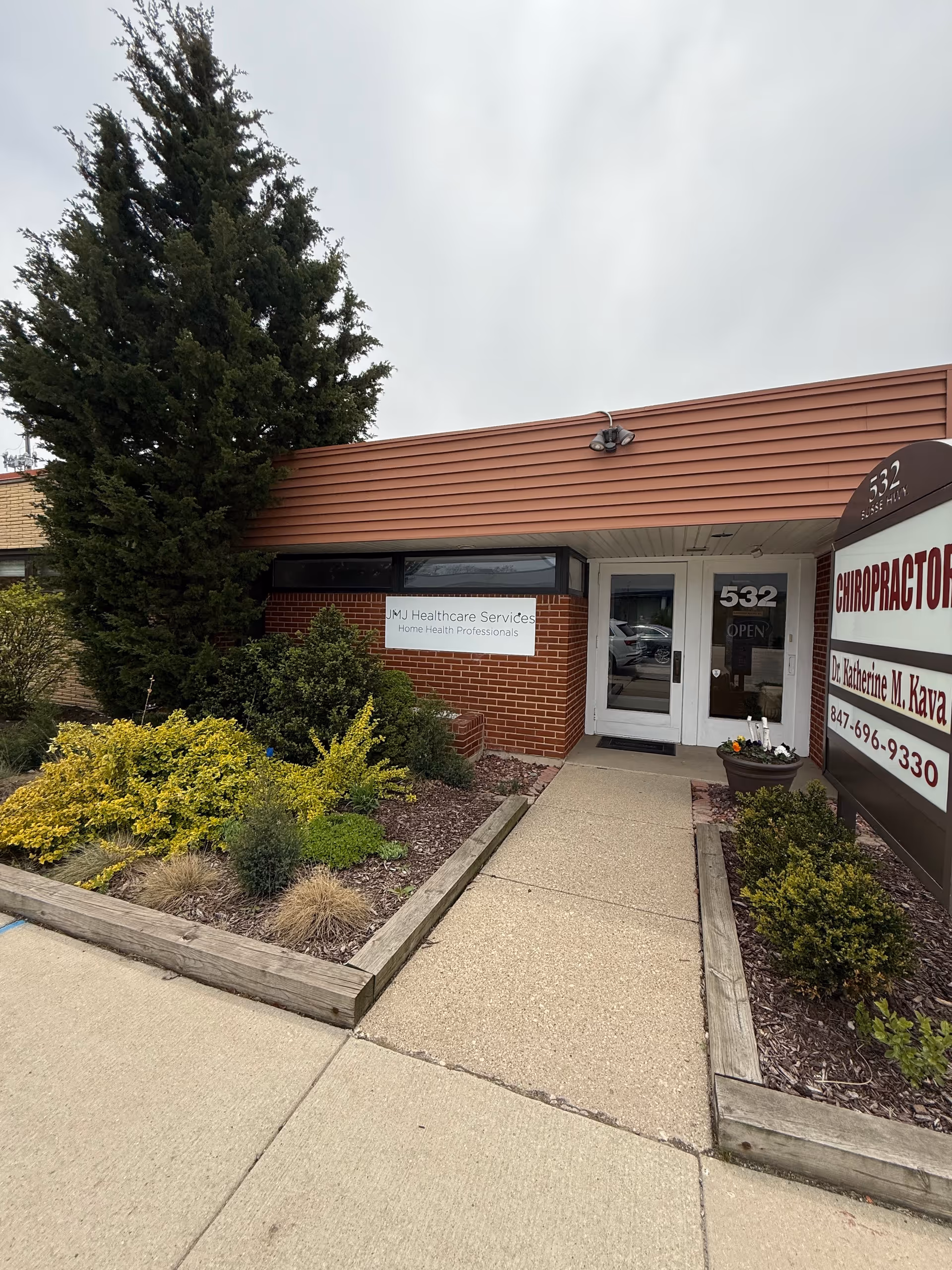 Facade of JMJ Healthcare Services building with a sidewalk and landscaped entry.