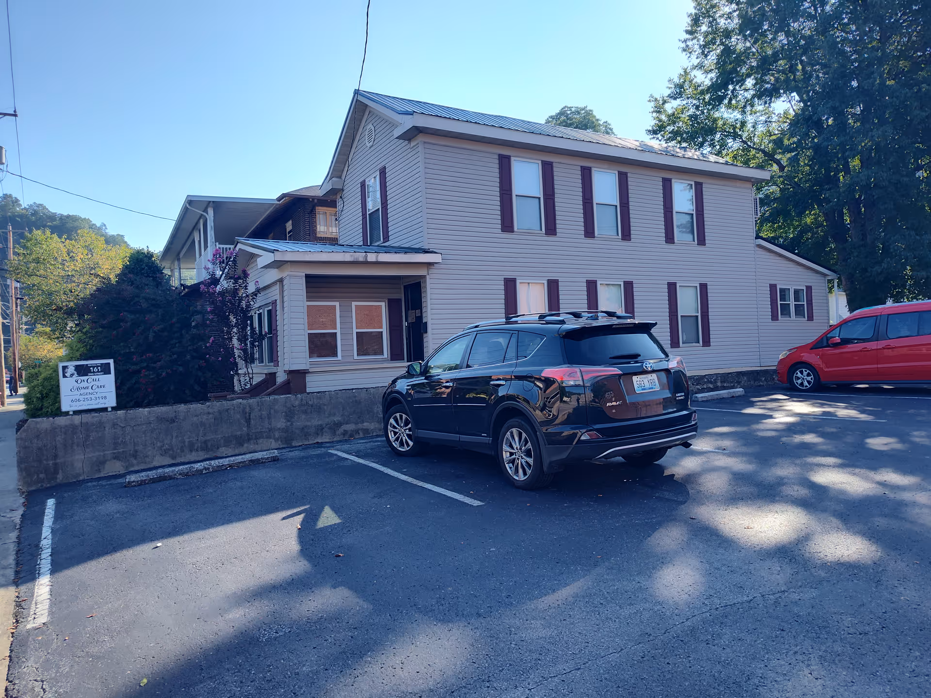 Two-story beige building with purple shutters, cars parked in a small lot outside.