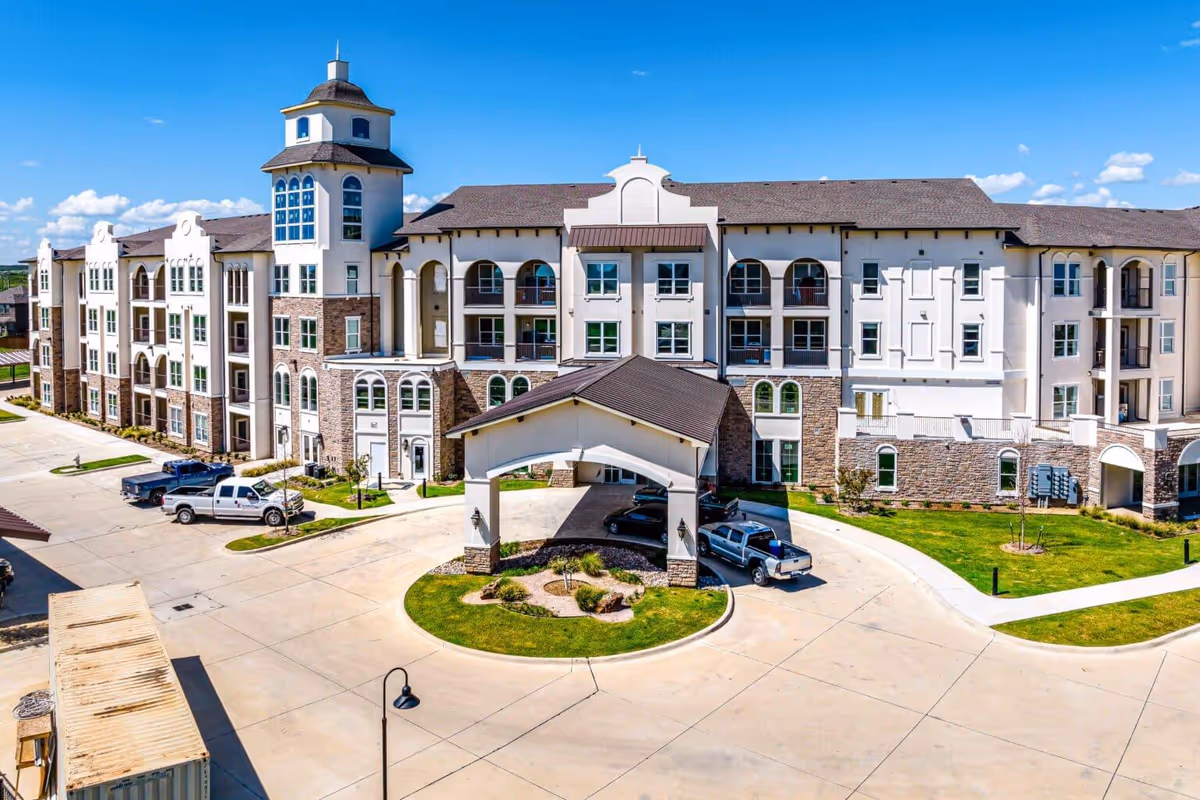 A large modern senior living building with a circular entrance drive and parked cars.
