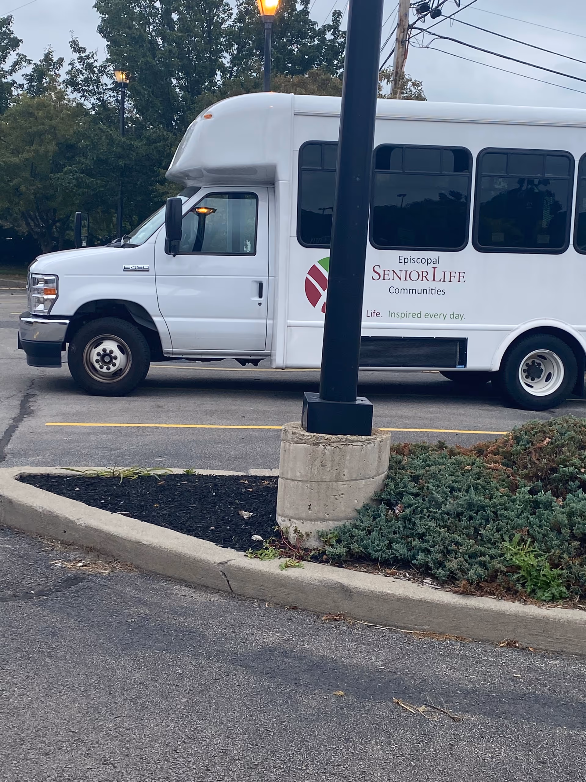 White bus with Episcopal SeniorLife branding parked beside landscaped area outdoors.