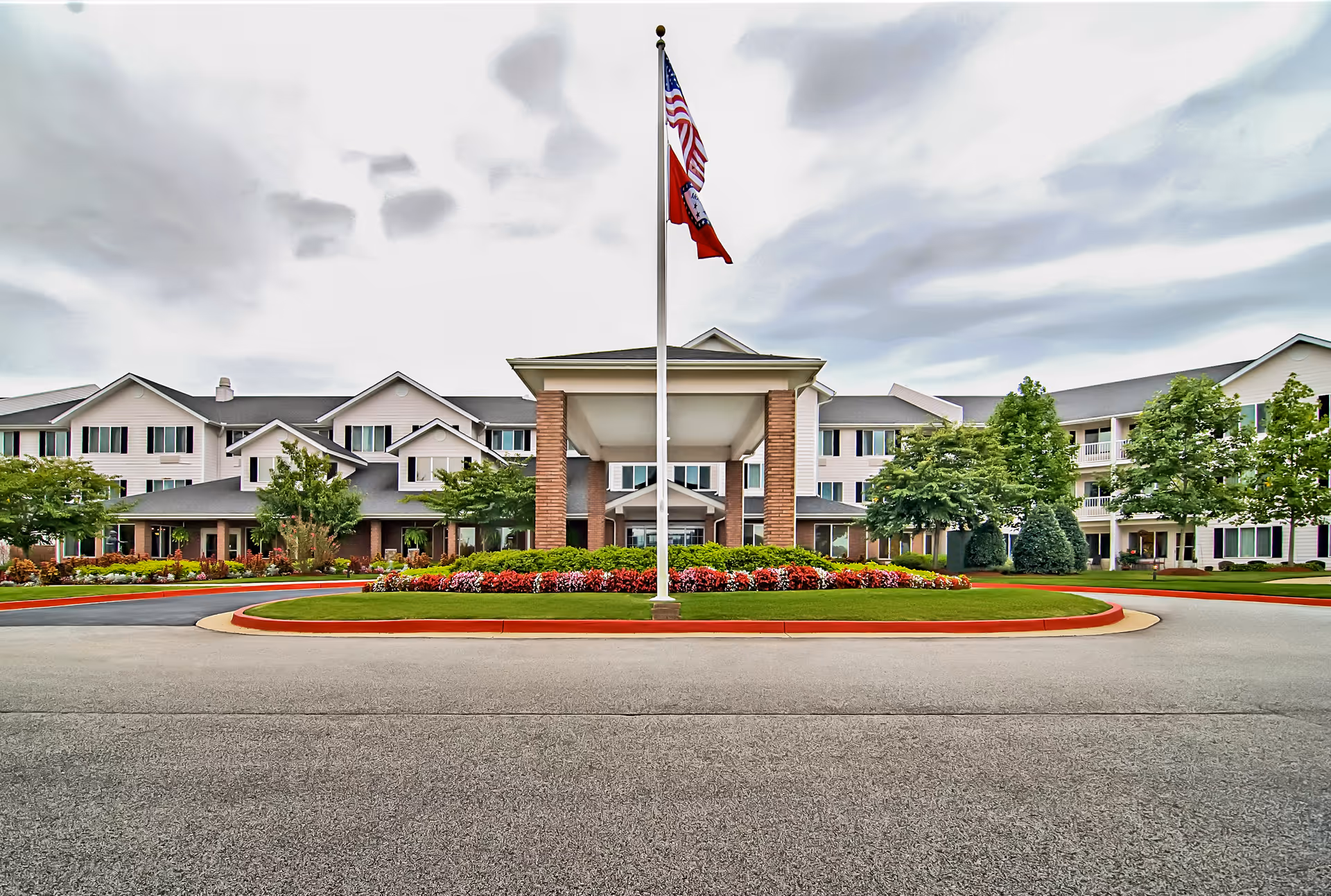 Exterior view of Morada Fort Smith senior living facility with flagpole and landscaped circular driveway.