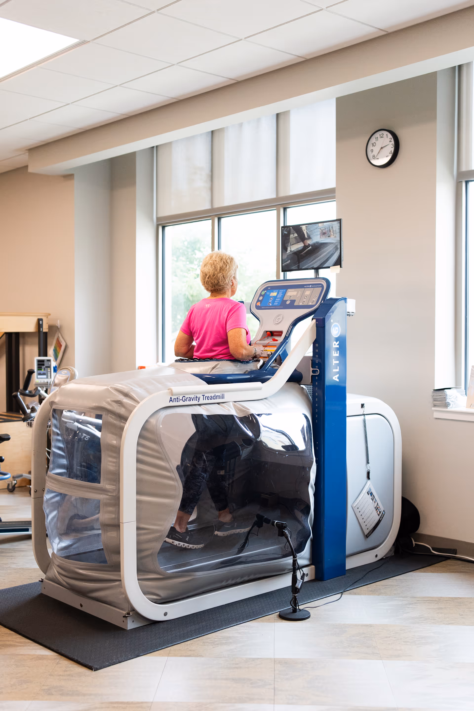 Senior woman uses an anti gravity treadmill in a bright rehabilitation gym area.
