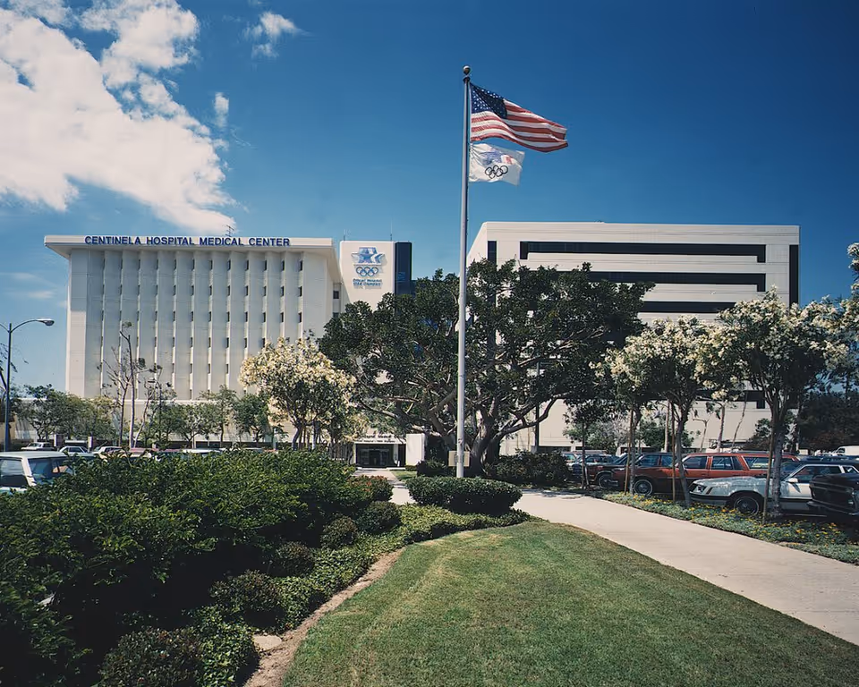A hospital building labeled Centinela Hospital Medical Center with flagpoles, trees, and a parking lot.
