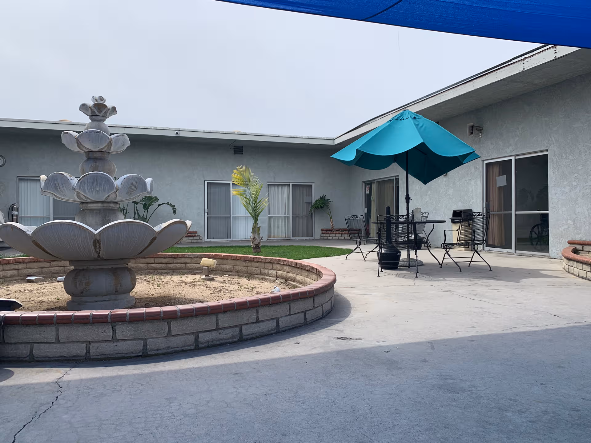 A circular fountain in a courtyard with outdoor seating and a blue umbrella.