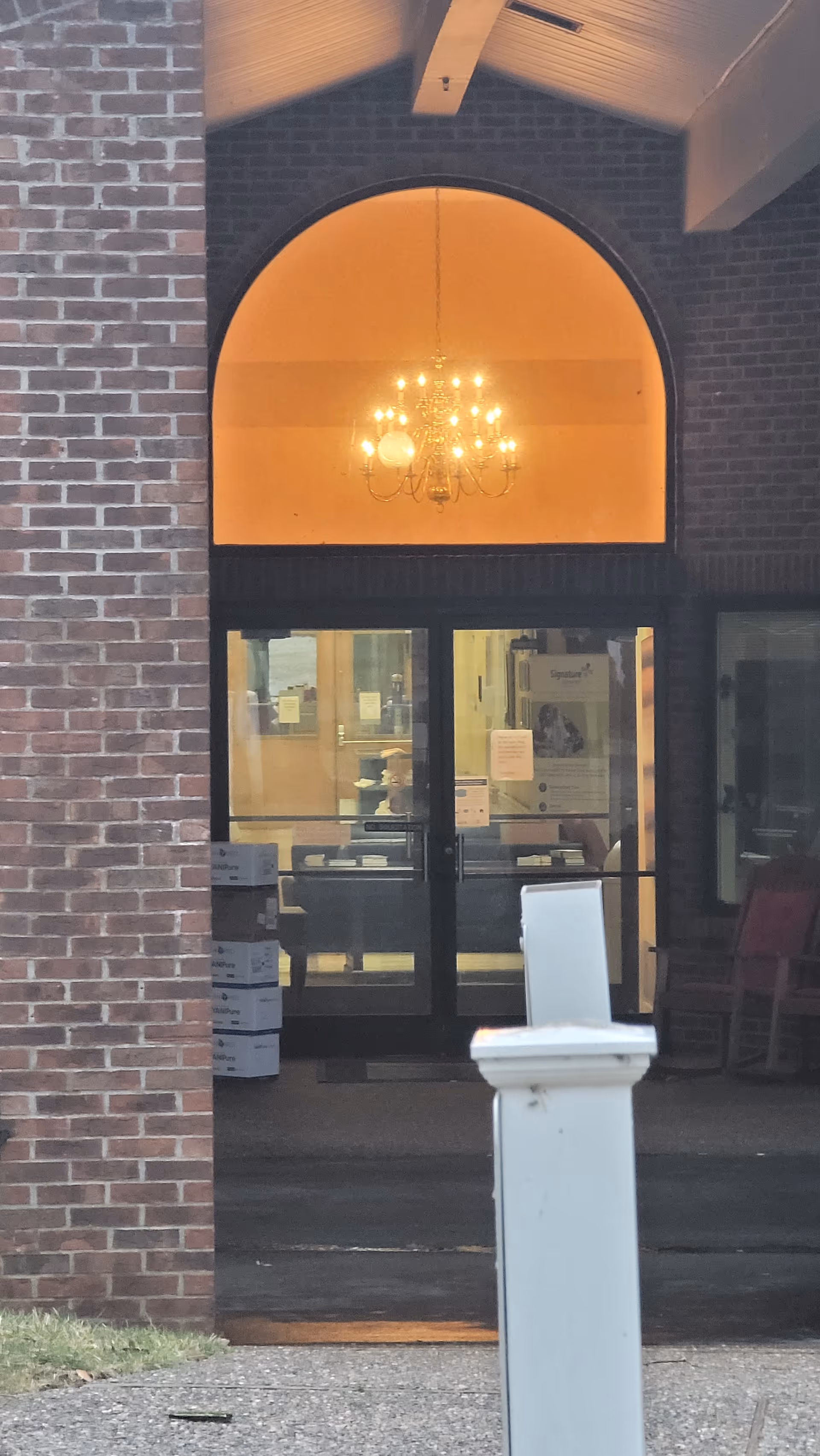 Brick building entrance with glass doors and a chandelier-lit lobby visible inside
