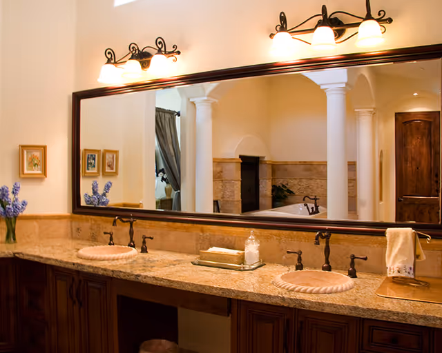 Spacious bathroom vanity with two sinks, a granite countertop, large framed mirror, and decorative wall lights.