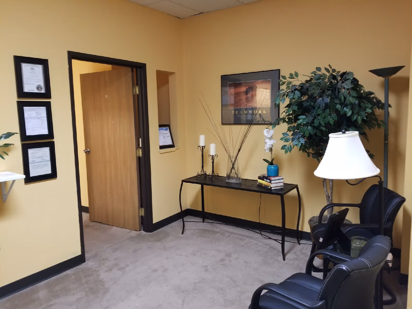 Yellow-walled reception area with a console table, decor, seating, and framed artwork.