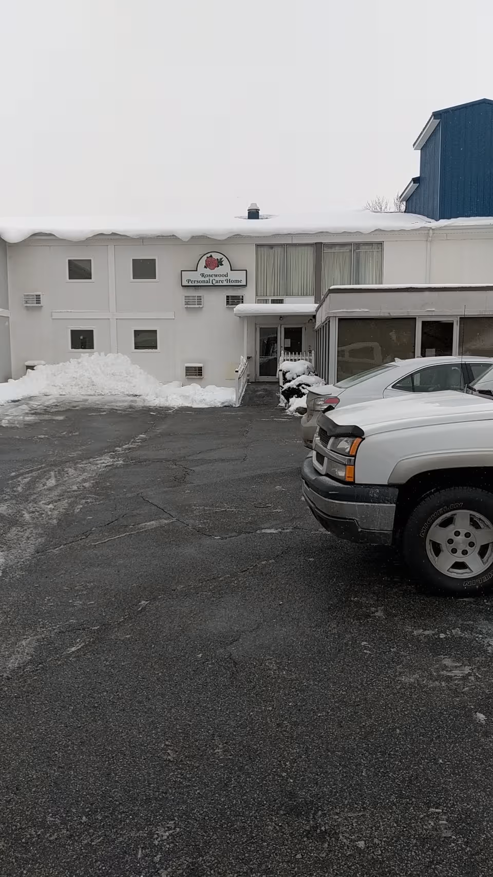 Exterior view of Rosewood Personal Care Home with snow, sign, and parked cars.