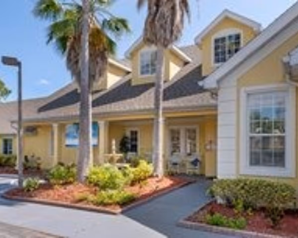 Exterior view of Brookdale Palm Coast building with yellow siding, large windows, and palm trees.