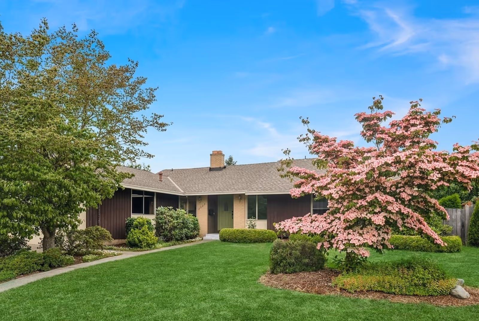 Single-story building front with green lawn, trees, and pink flowering tree.