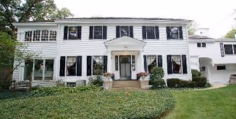 White two-story building exterior with black shutters and a central entrance.