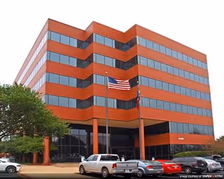 Red-orange multi-story building with an American flag and cars parked in front.