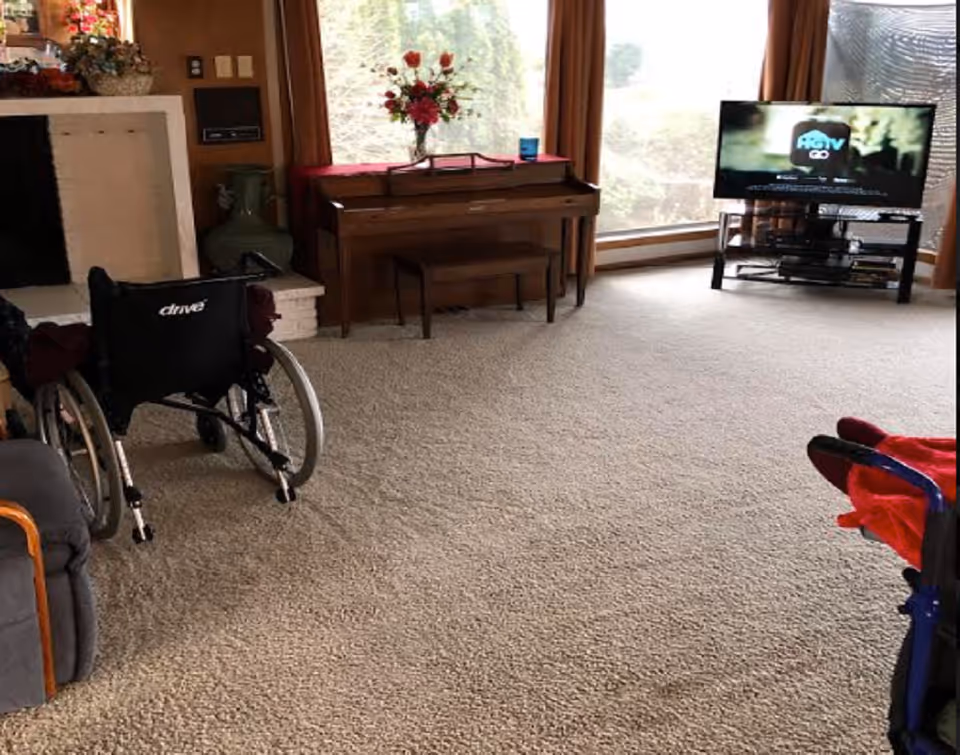 Living room at Bay Bridge Care Home featuring wheelchair, piano, and TV.