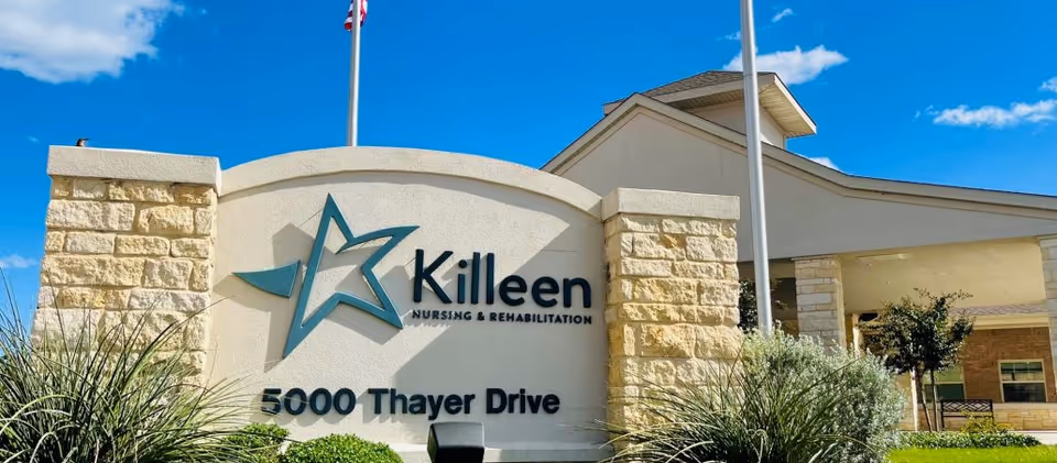 Stone entrance sign reading "Killeen Nursing & Rehabilitation 5000 Thayer Drive" with landscaping and the facility building under a blue sky.